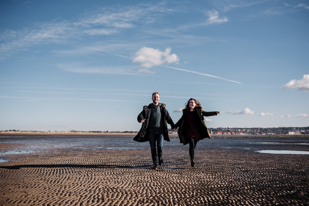 Fun shot of couple running on the beach together. West Kirby engagement photography