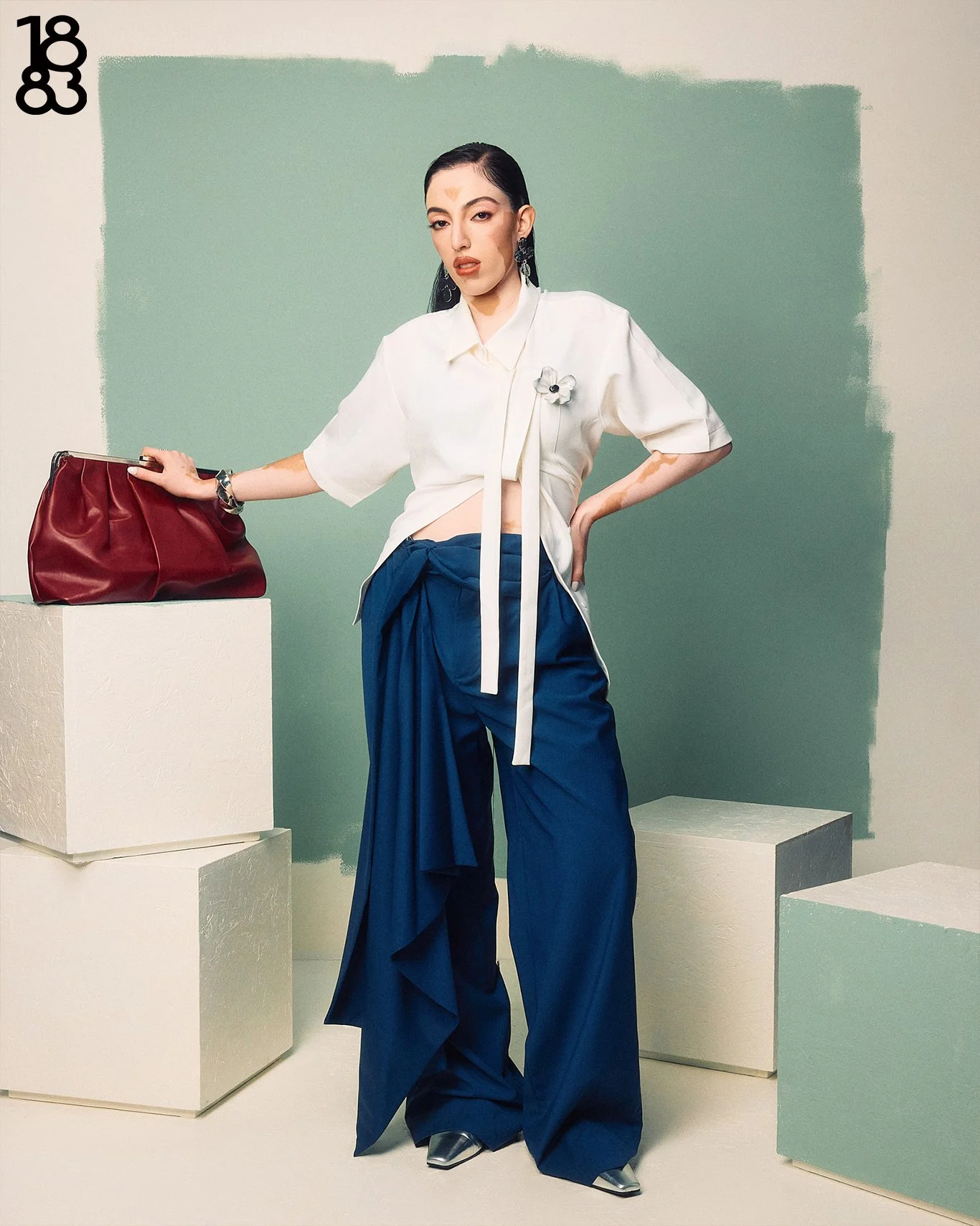 Fashion photography in London of woman with vertiligo, blue pants and white top red bag on aqua studio set design
