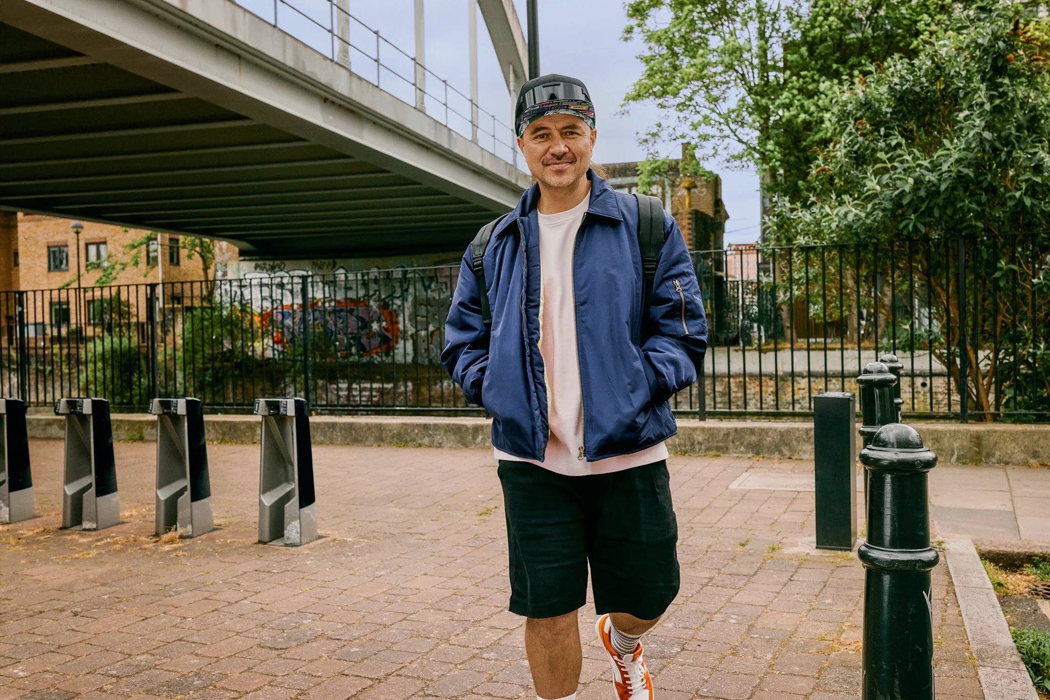 Advertising photography and street photography in London for IBM billboard OOH ad campaign for Wimbledon tennis tournament with lifestyle street photography of sneaker influencer walking with confident smile under bridge with sunglasses on his cap