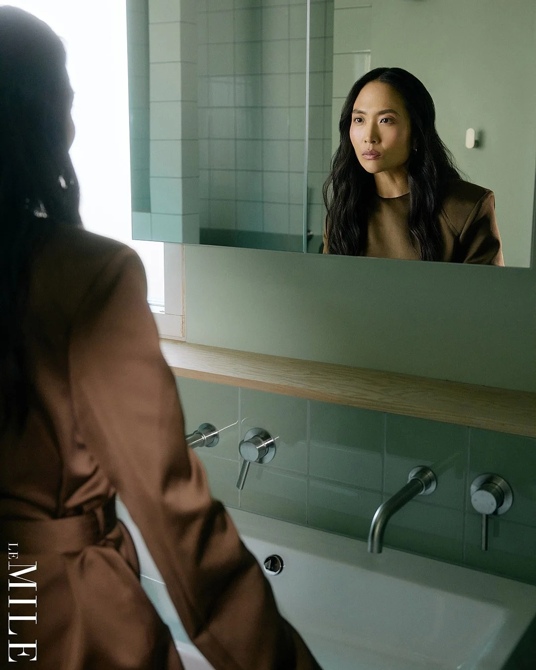  Commercial lifestyle photographer in London captures editorial fashion photography of actress Sandra Yi Sencindiver in styled bathroom wearing brown outfit looking at self in mirror 