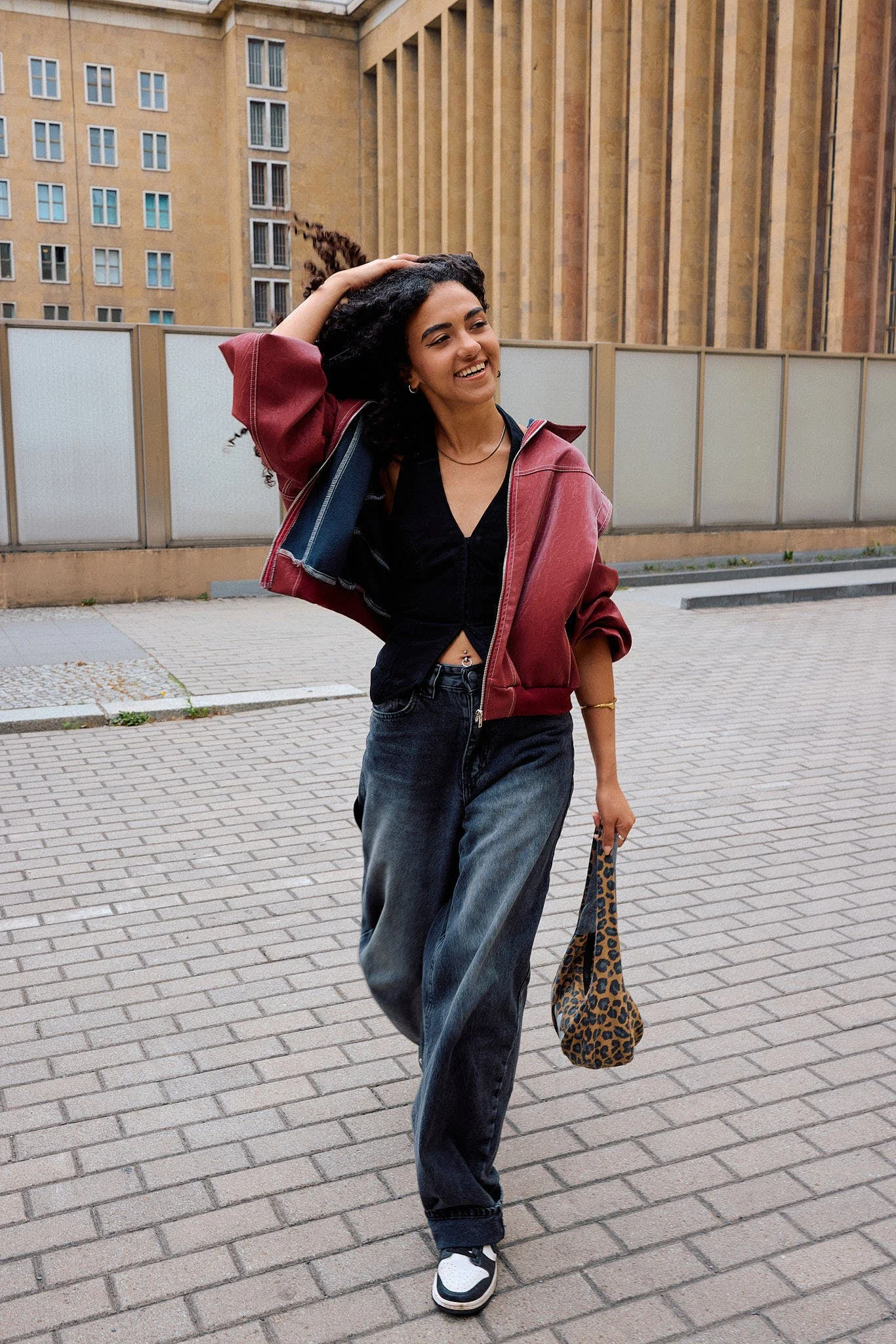  Burgundy cropped track jacket over a black corset top with washed black baggy jeans, leopard-print shoulder bag and Nike trainers, sport-luxe with animal print, outside a limestone colonnade, Berlin Fashion Week SS27 