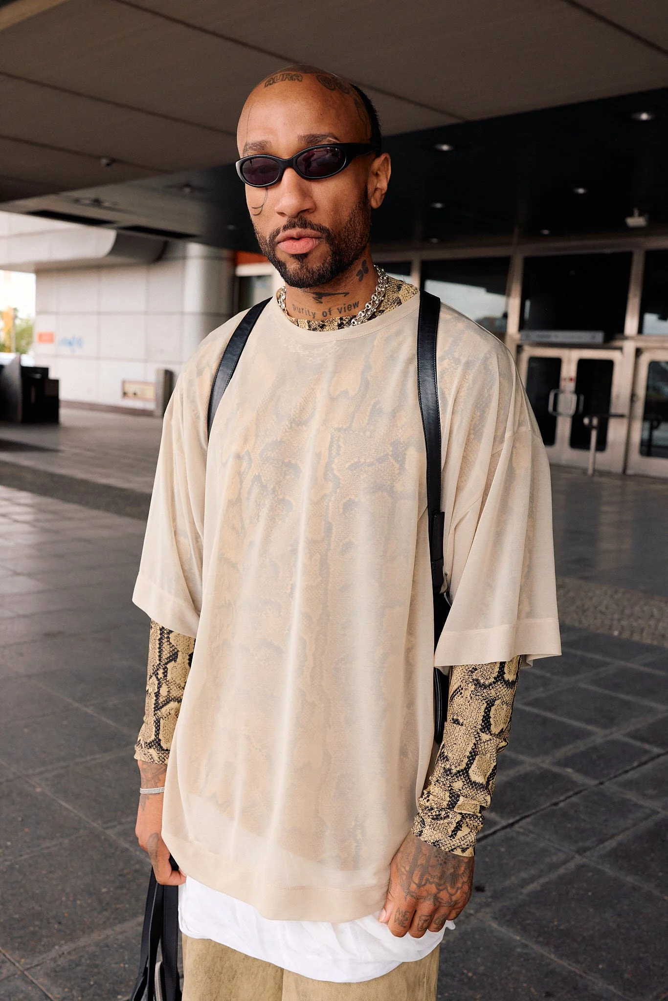  Guest in a sheer python-print oversized tee layered over a snakeskin long-sleeve top with khaki trousers and a black leather strap bag, animal print, outside a show entrance, Berlin Fashion Week SS27 