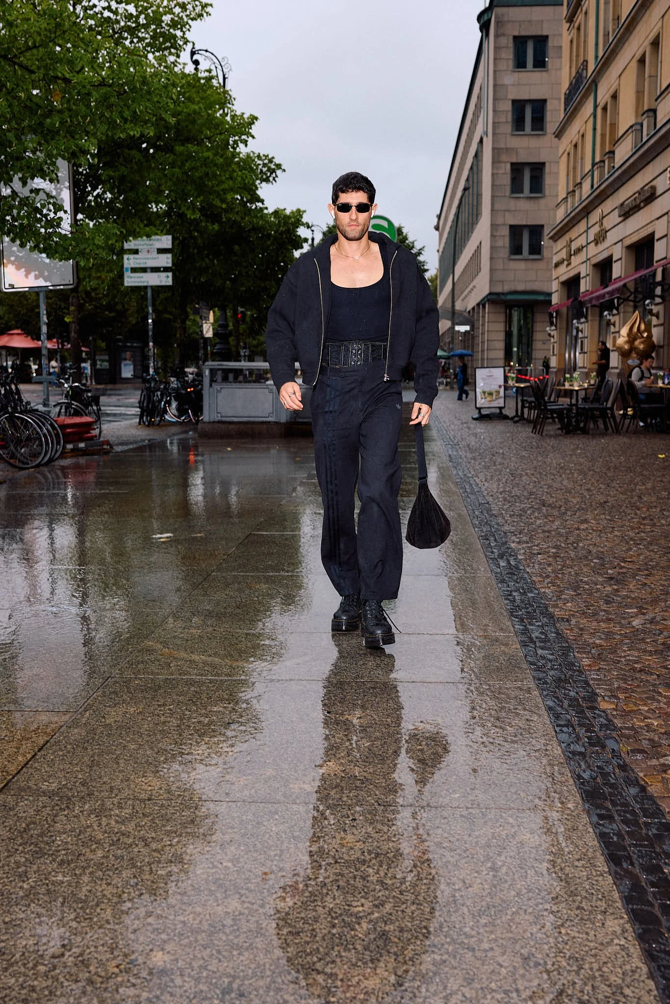  Navy zip bomber over a scoop-neck bodysuit with a corset belt and adidas three-stripe trousers with chunky lace-up boots, sport-luxe menswear, on rain-slicked pavement by an S-Bahn sign, Berlin Fashion Week SS27 