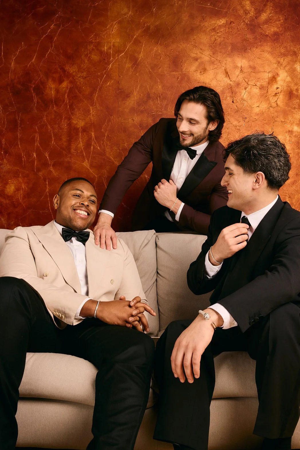 Advertising photographer London campaign image of men dressed in suits wearing bracelets before wedding on sofa with orange wall background for jewellry brand DOLA.