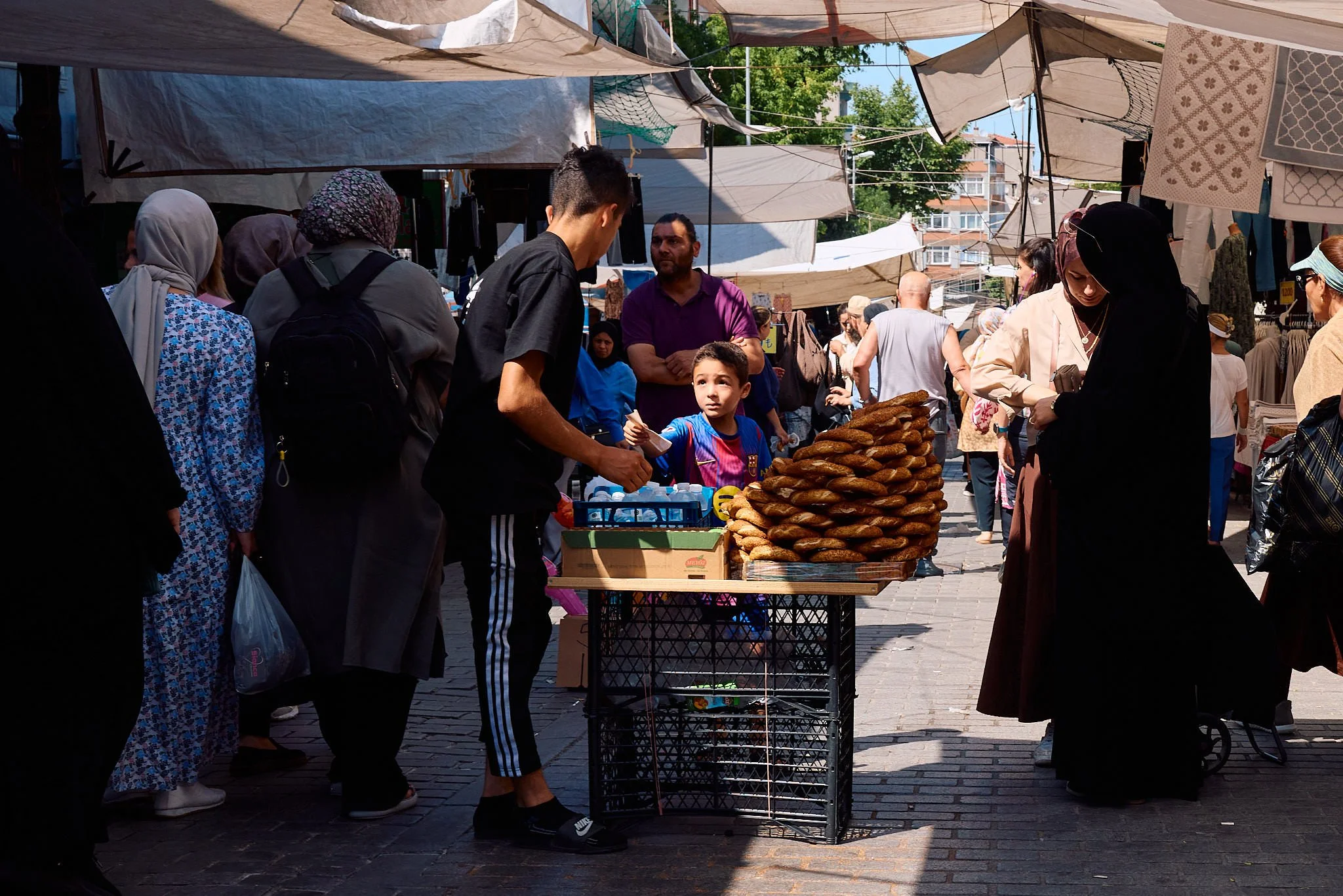 Young simit seller arranging rings of sesame bread on a cart in the crowd at Istanbul’s Wednesday market