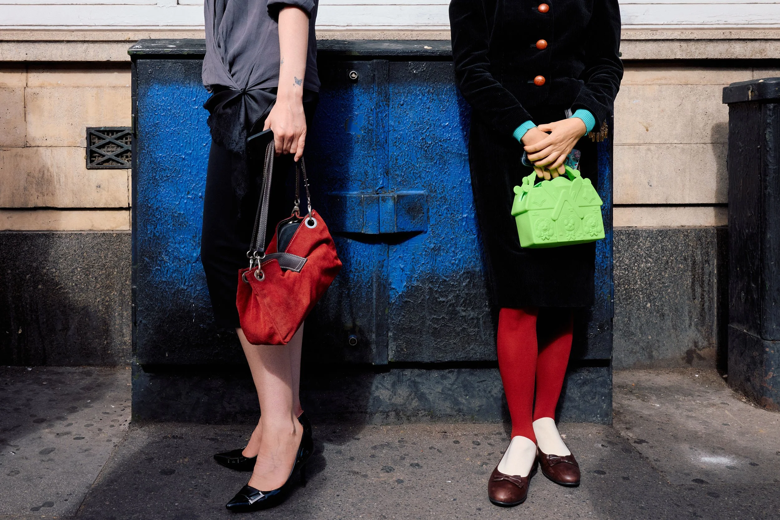 Two London Fashion Week guests from the waist down, red tights and a green house-shaped bag next to a red suede tote
