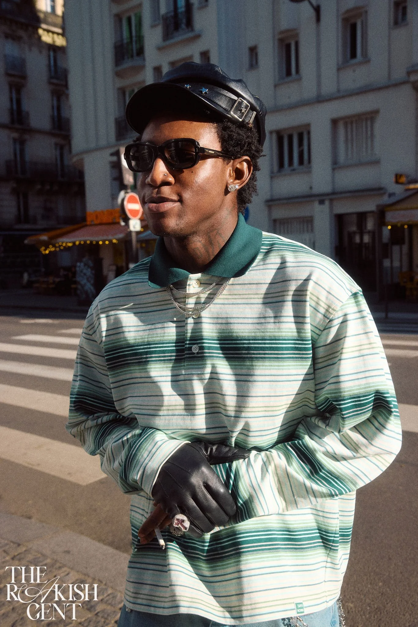 Editorial portrait of Lagos-based music artist Shallipopi in a leather cap and striped polo on a Paris street