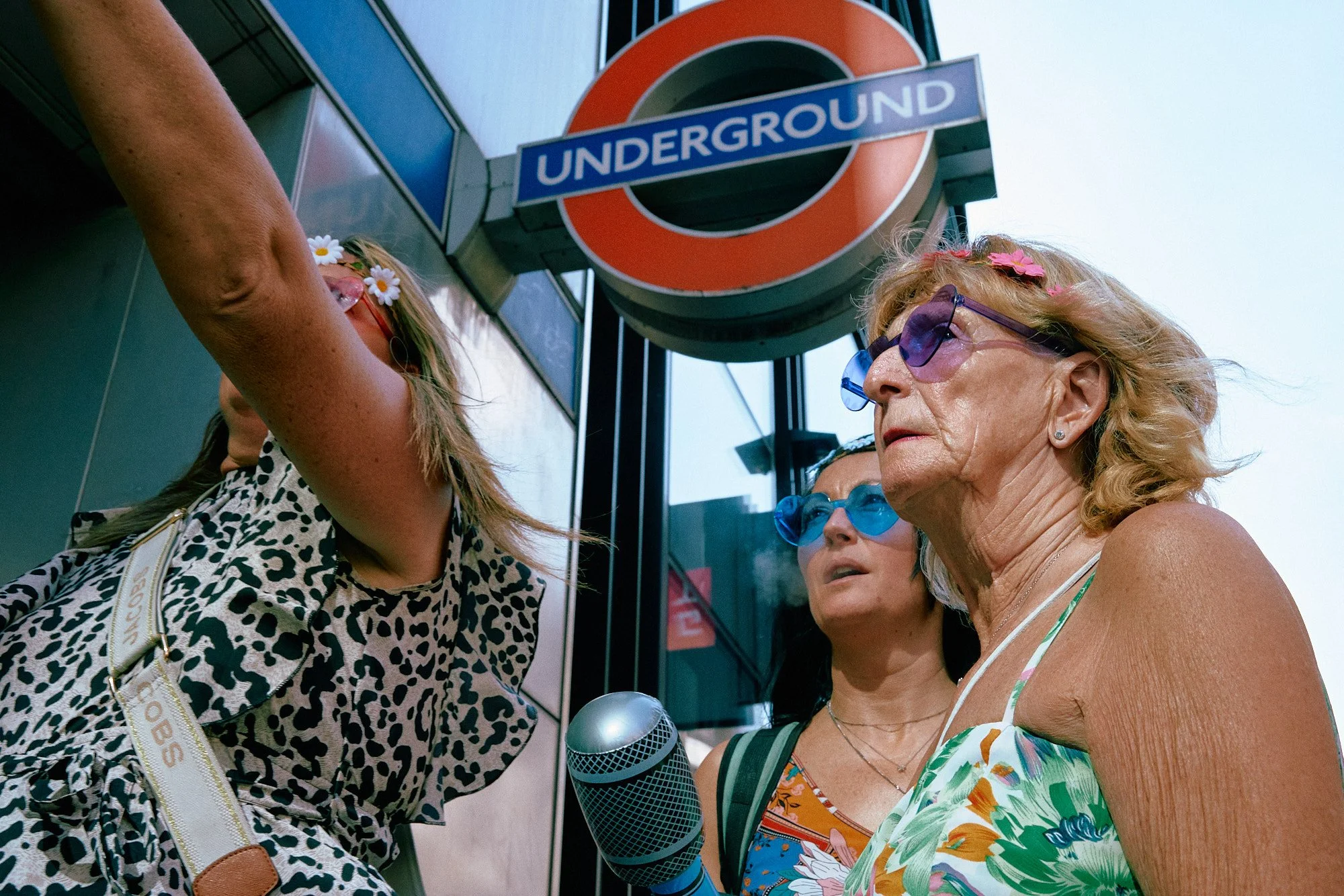 Street photography in London, UK of three women exiting tub station wearing sunglasses under Underground sign looking off