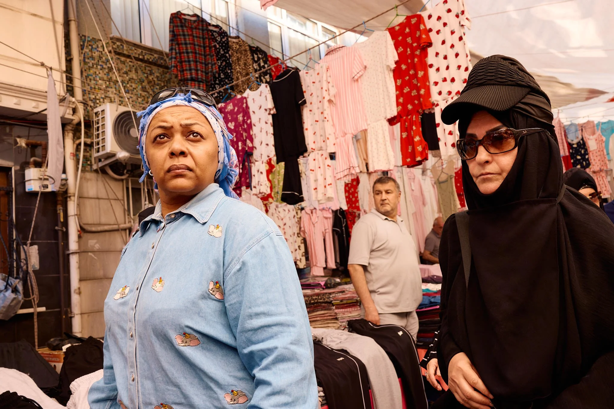 Woman in a blue headscarf and denim shirt walking past rails of dresses at the Wednesday market in Fatih, Istanbul