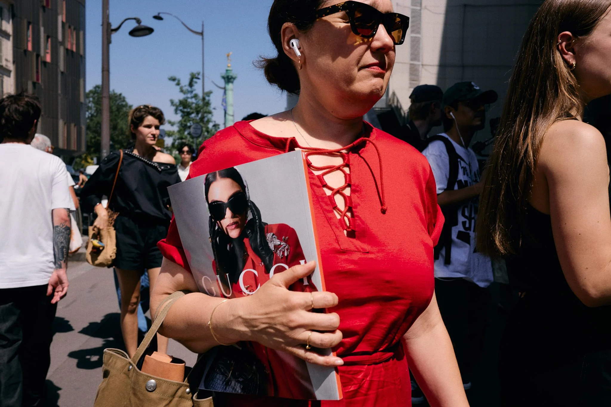 Woman in a red lace-up dress holding a Gucci magazine with a matching red cover look outside the Lemaire show, Paris Fashion Week SS27 menswear