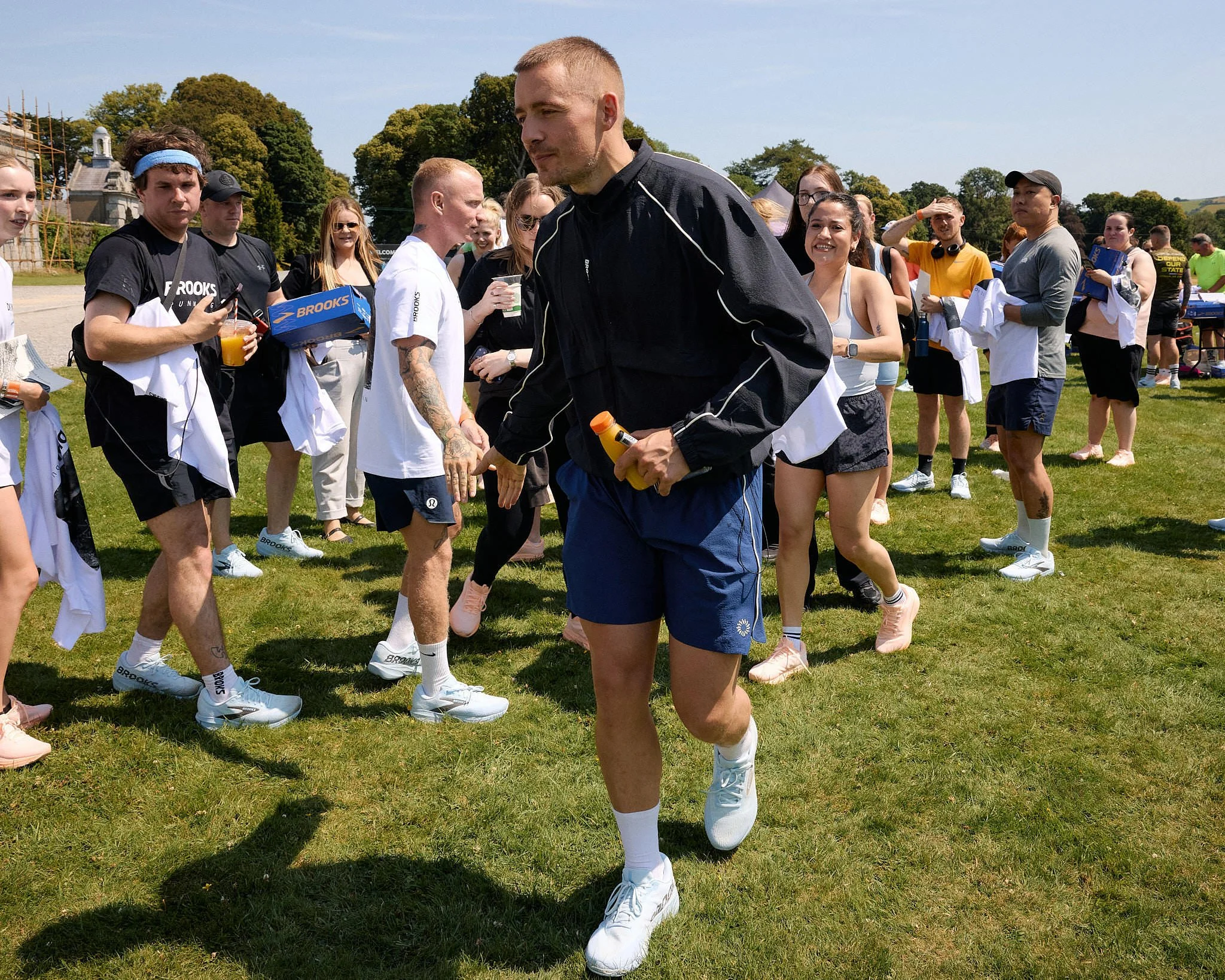 Dermot Kennedy walking through a crowd of DK5K runners on the lawn after the race, holding an orange drink bottle