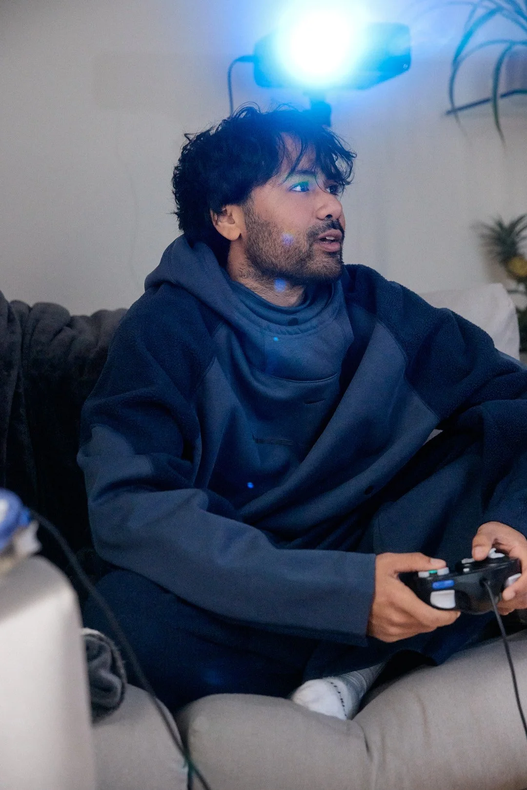 Dating profile photography portrait of man with messy hair playing Gamecube on sofa with projector light beam above head holding controller
