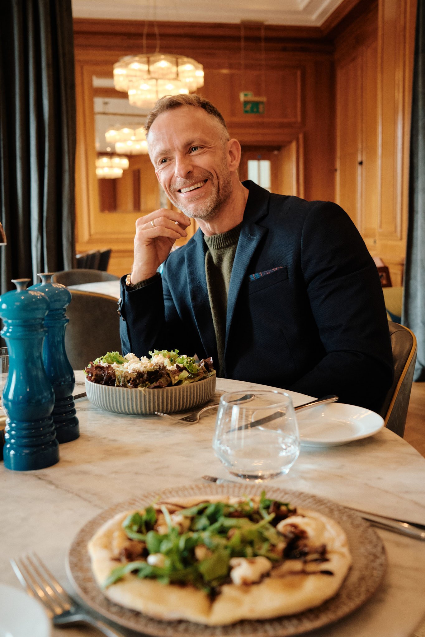 London dating profile photography of a man laughing over lunch in a wood-panelled restaurant.
