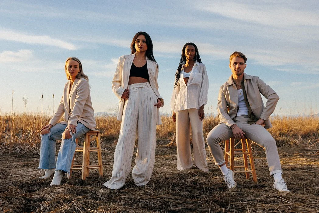Fashion photographer London lifestyle editorial image of four models, male and female, standing in an open field with dried grass styled in cream and white at golden hour for a spring summer editorial.