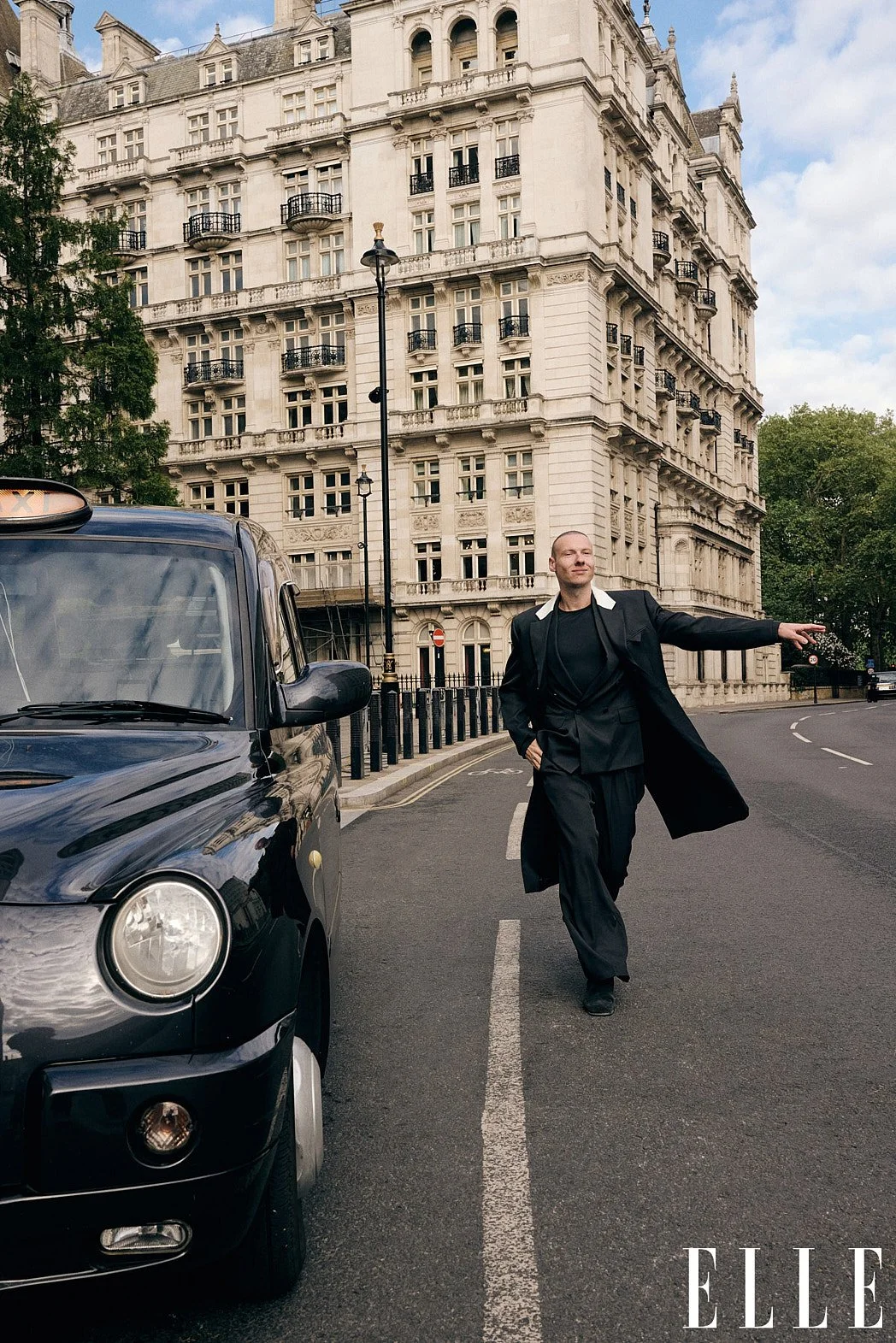 Personal branding street style fashion photography of fashion consultant Bernard Garby hailing a taxi on historical street with long black jacket and black cab on left for ELLE magazine editorial
