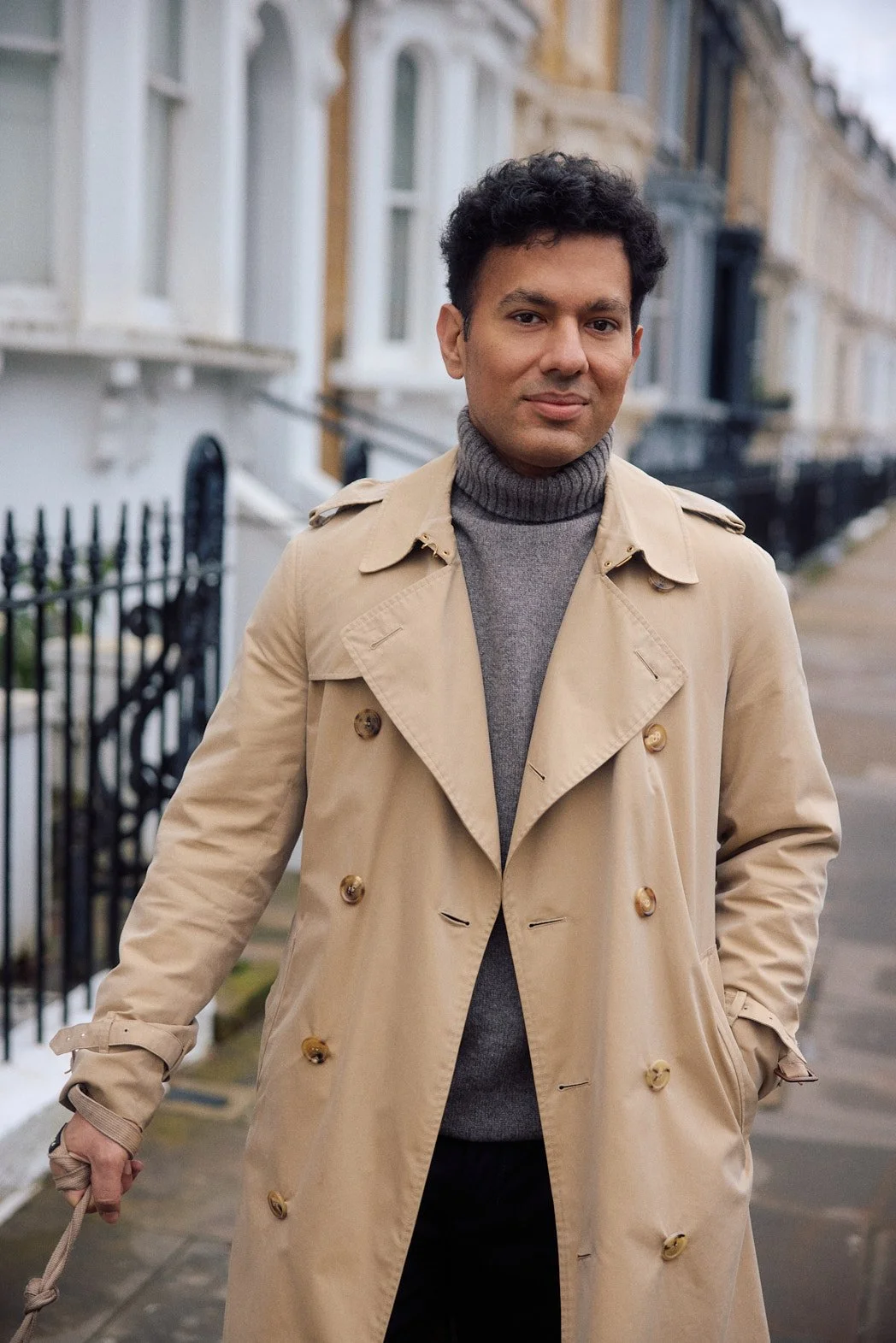 Dating photography in London of man in brown trench coat with grey turtleneck walking dog looking at camera with confident expression