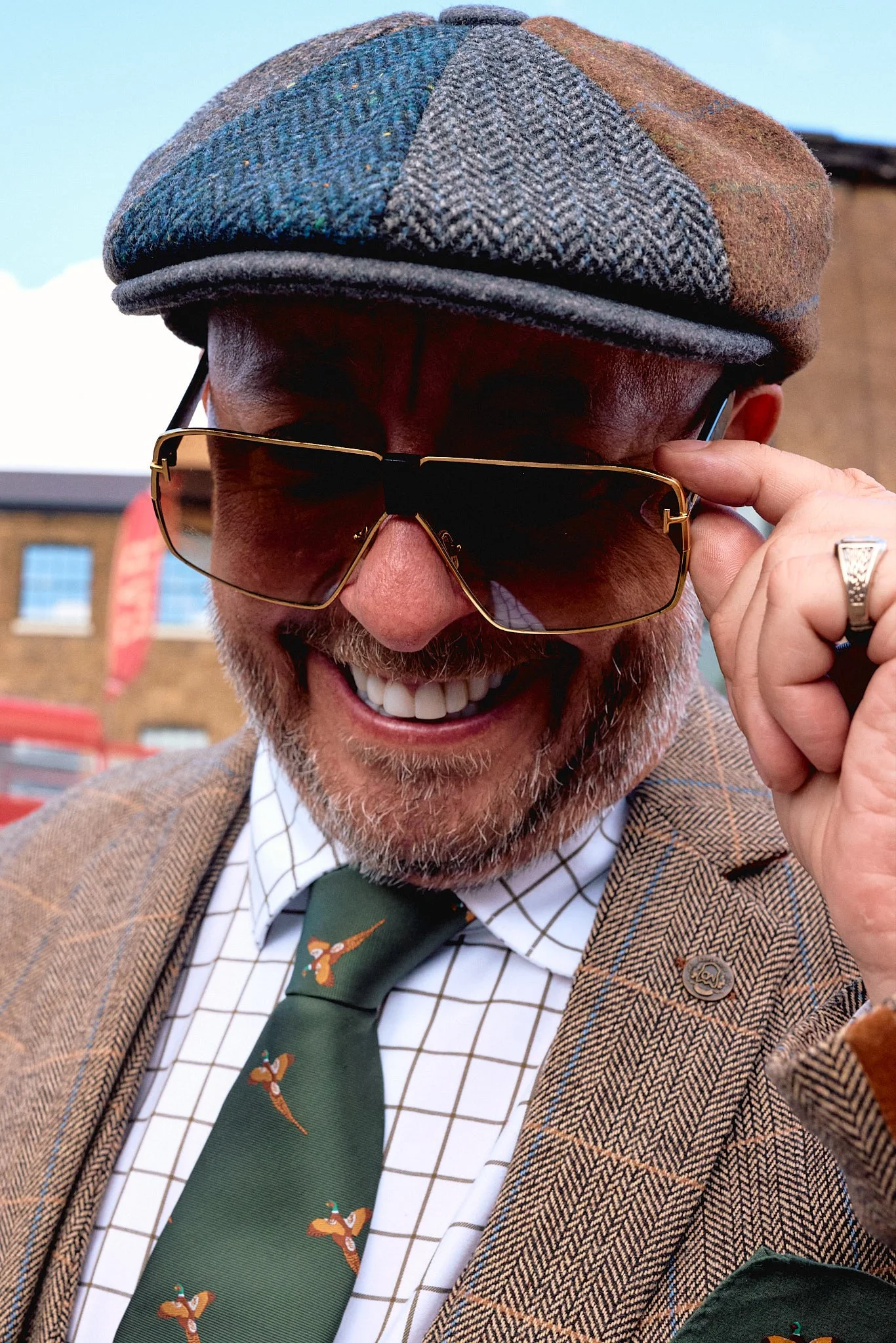 Street photography in London of man in tweed suit smiling with veneer teeth and dark sunglasses with bus in background