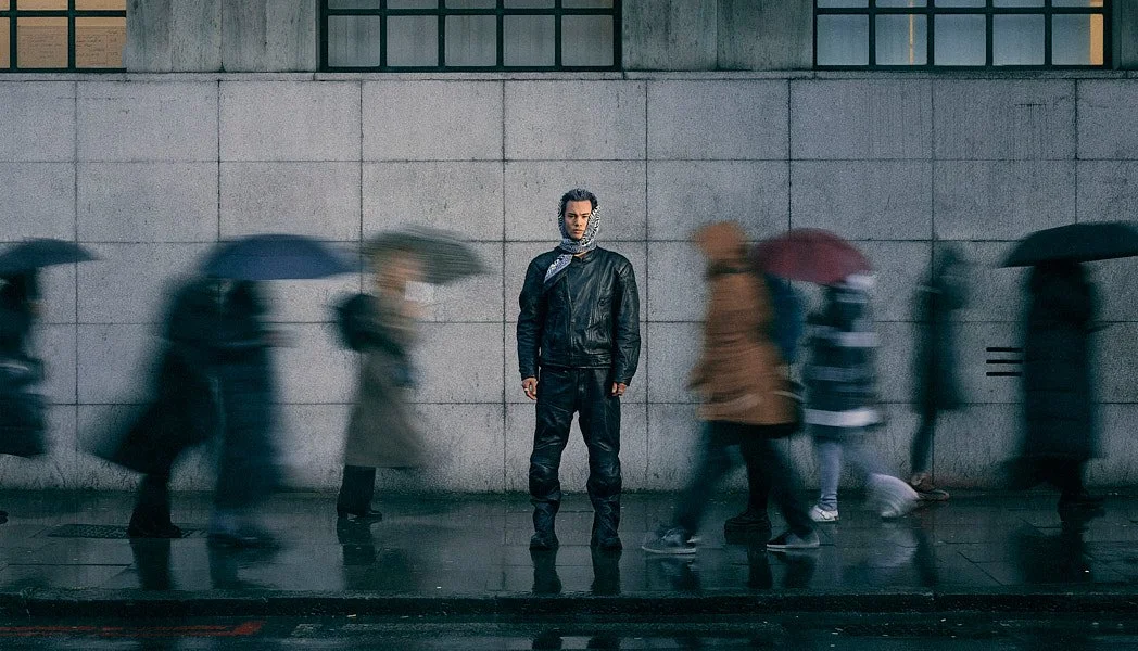 Fashion photographer London street style editorial portrait for album cover of music artist Luvrite standing still across street wearing leather and head scarf while pedestrians motion blur.