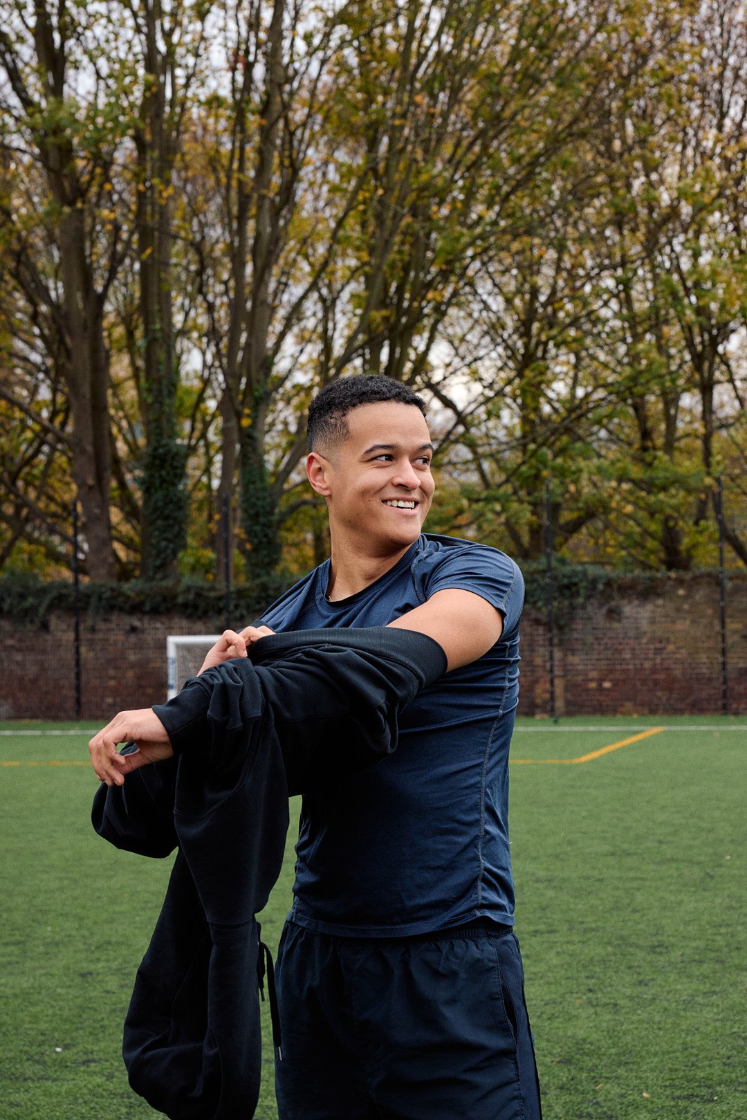 Dating profile photography in London of light skin man taking off hoodie on football pitch portrait