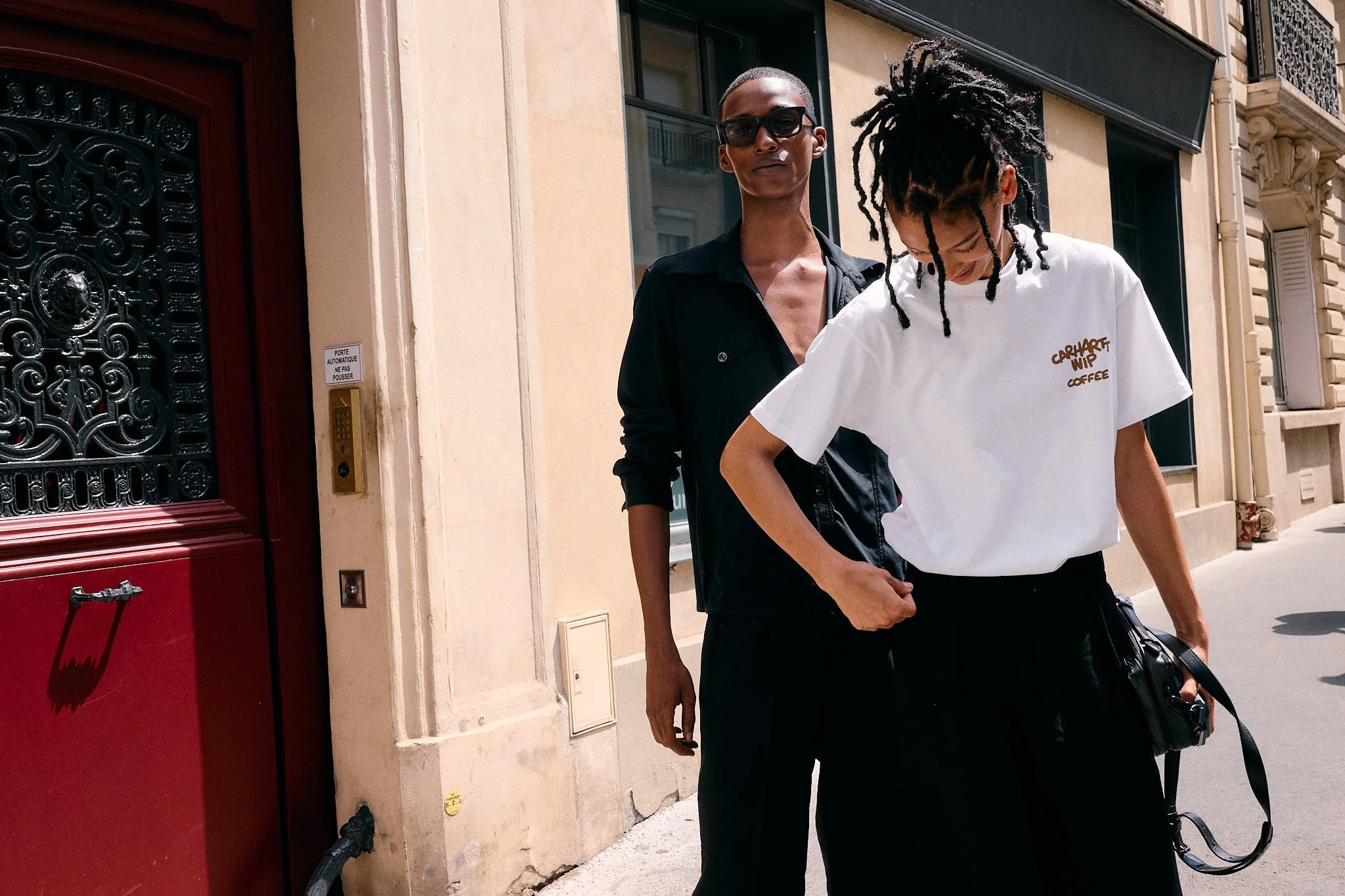 Two guests in black tailoring and a white Carhartt WIP graphic T-shirt outside the Sacai show, Paris Fashion Week SS27 menswear
