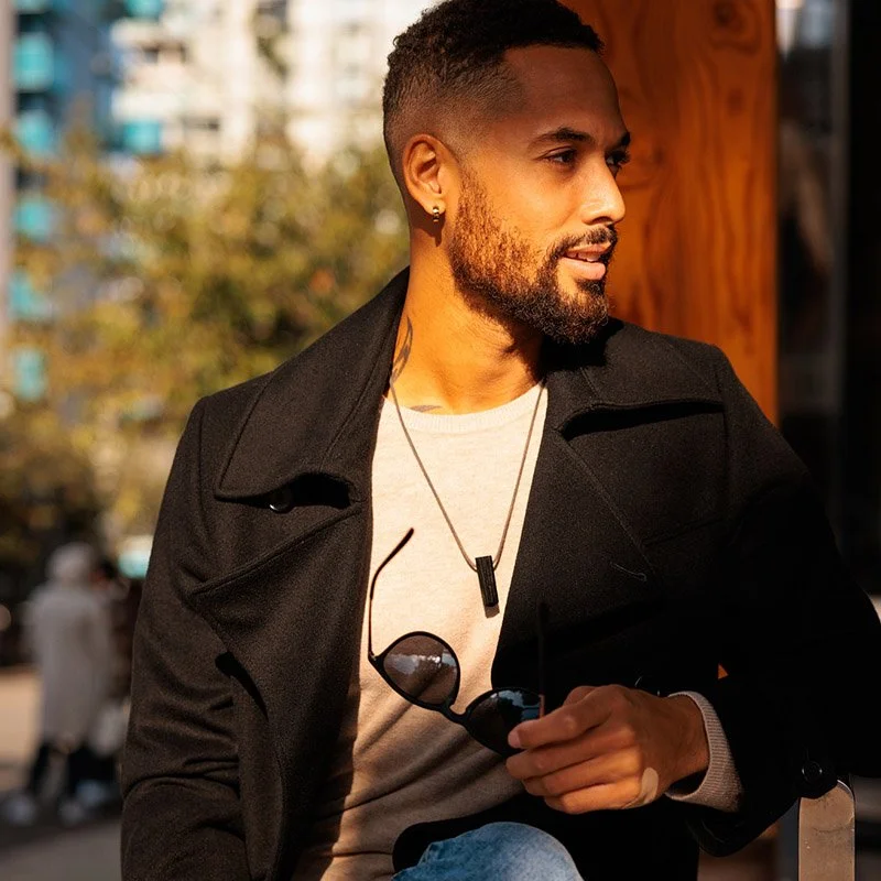 Dating photography in London of a man holding sunglasses looking off into the sunset black jacket and beard, dark skin