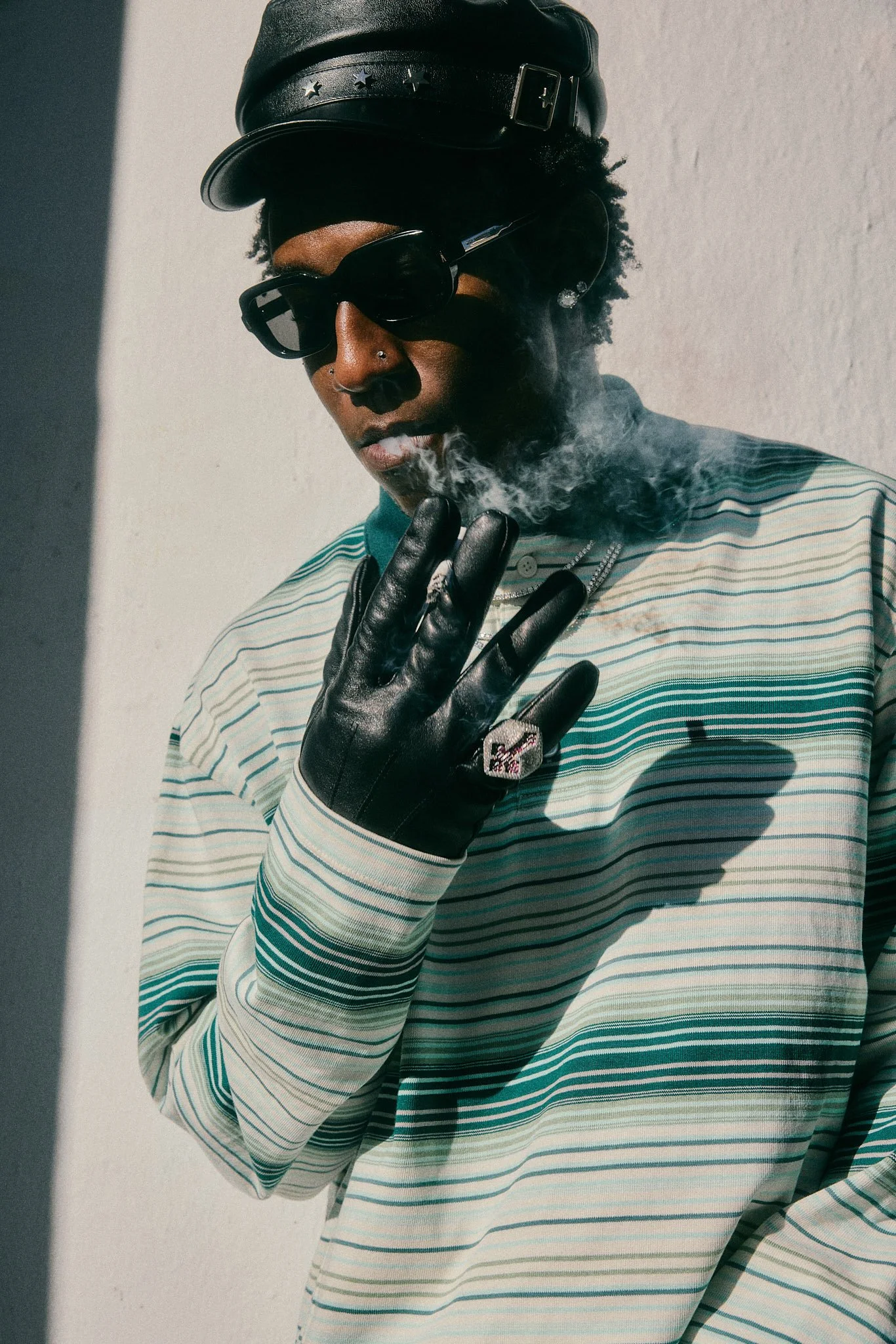 Editoirial fashion photography with Lagos, Nigeria music artist Shallipopi at Paris Fashion Week AW26 street style photoshoot wearing leather hat, sunglasses, green striped rugby shirt, black leather gloves and diamond rings