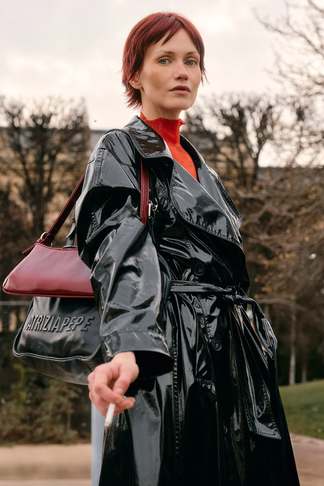 Street style fashion photography at Paris Fashion Week womenswear FW26 by London street photographer of woman in glossy black trench coat and red turtleneck with two purses
