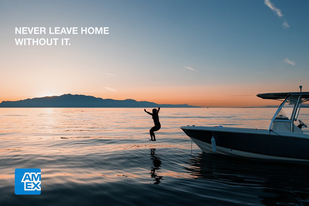 Advertising photographer London campaign image for speculative American Express ad of silhouette actress jumping off boat into ocean at sunset with mountains in background.