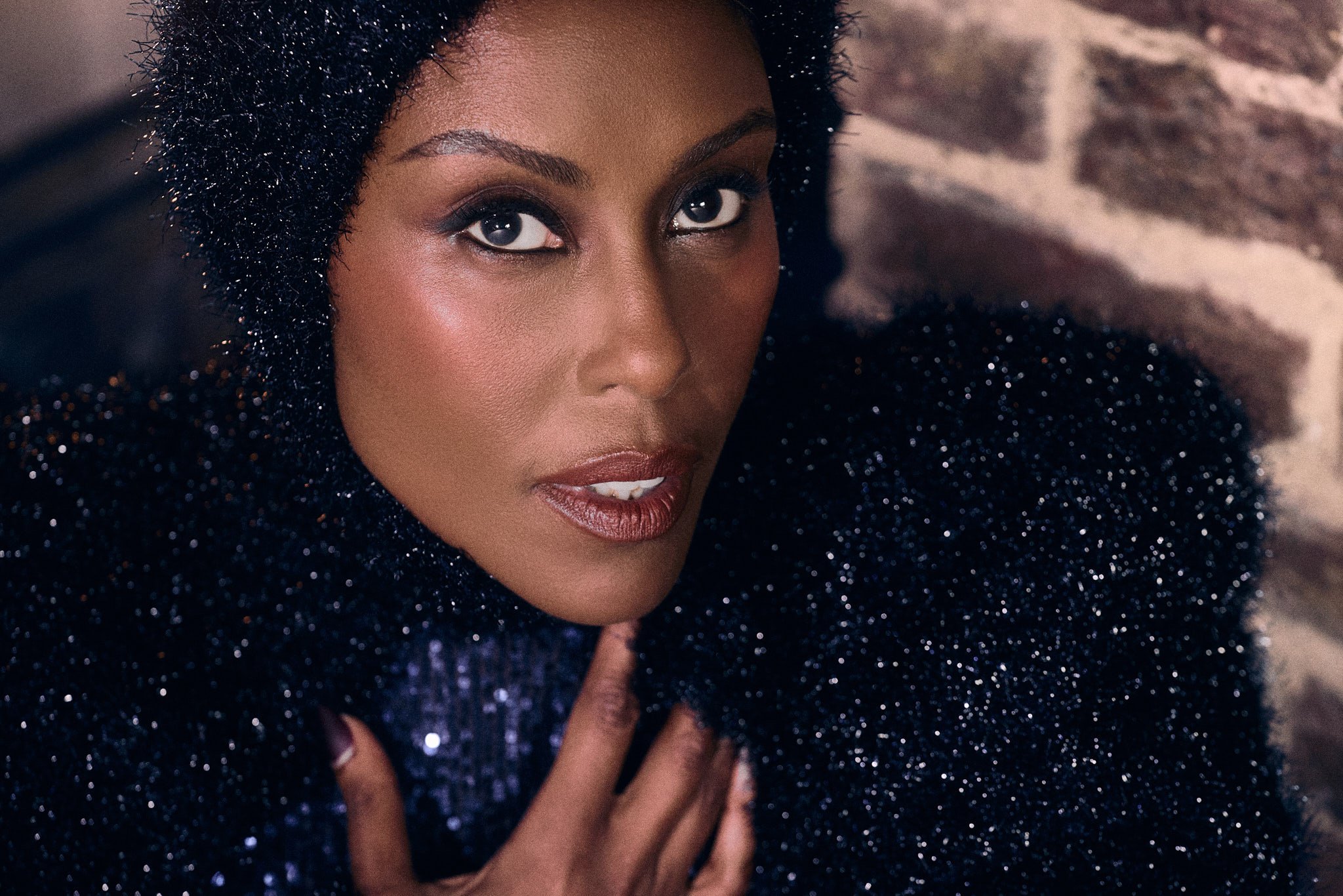 Commercial lifestyle photographer in London captures editorial fashion photography of Apple TV’s Hijack series star Christine Adams seated in front of brick fireplace looking at camera close up with textured head covering for LE MILE magazine cover