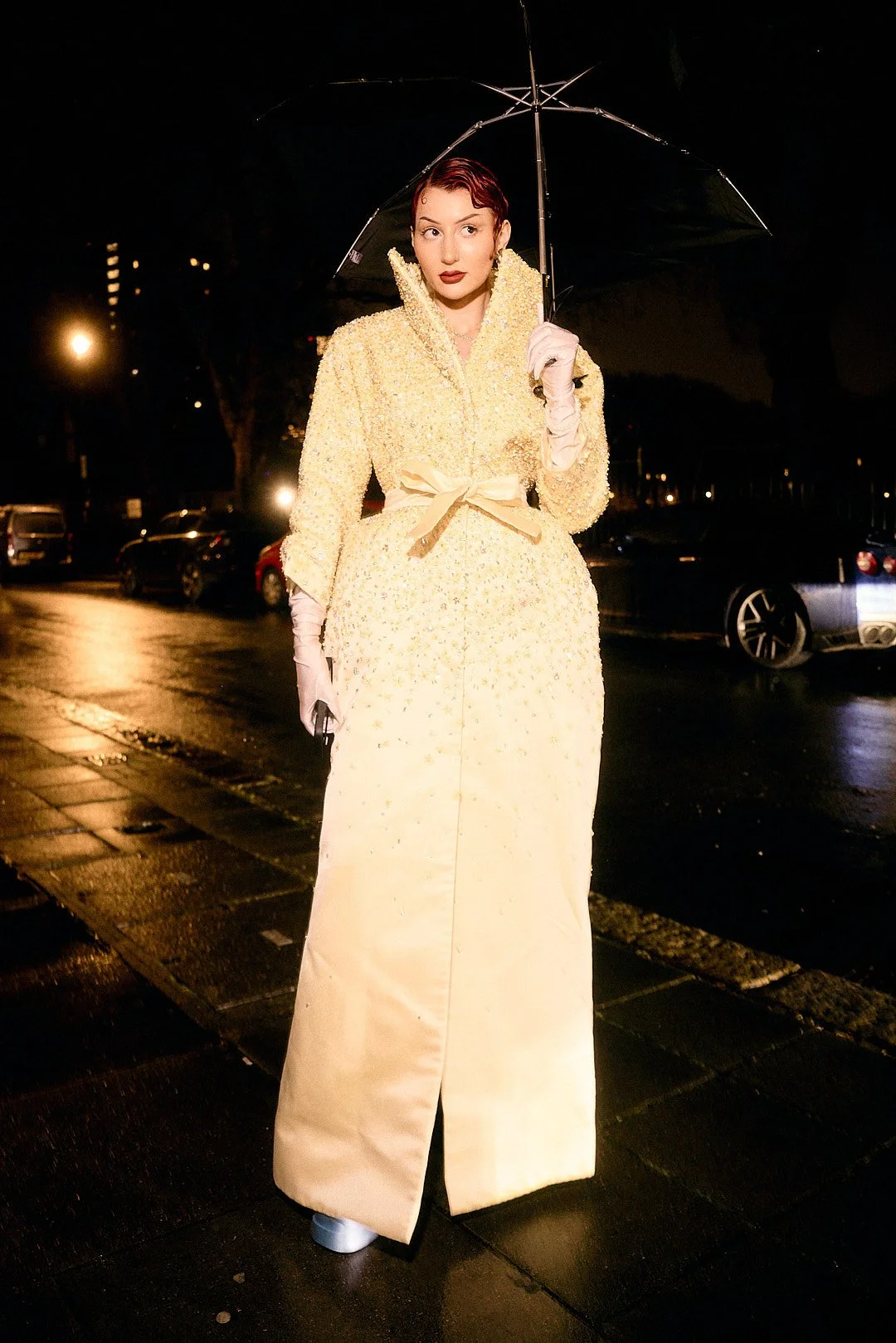 Street style portrait of Eve Lily at London Fashion Week wearing yellow dress and umbrella in rain flash photo