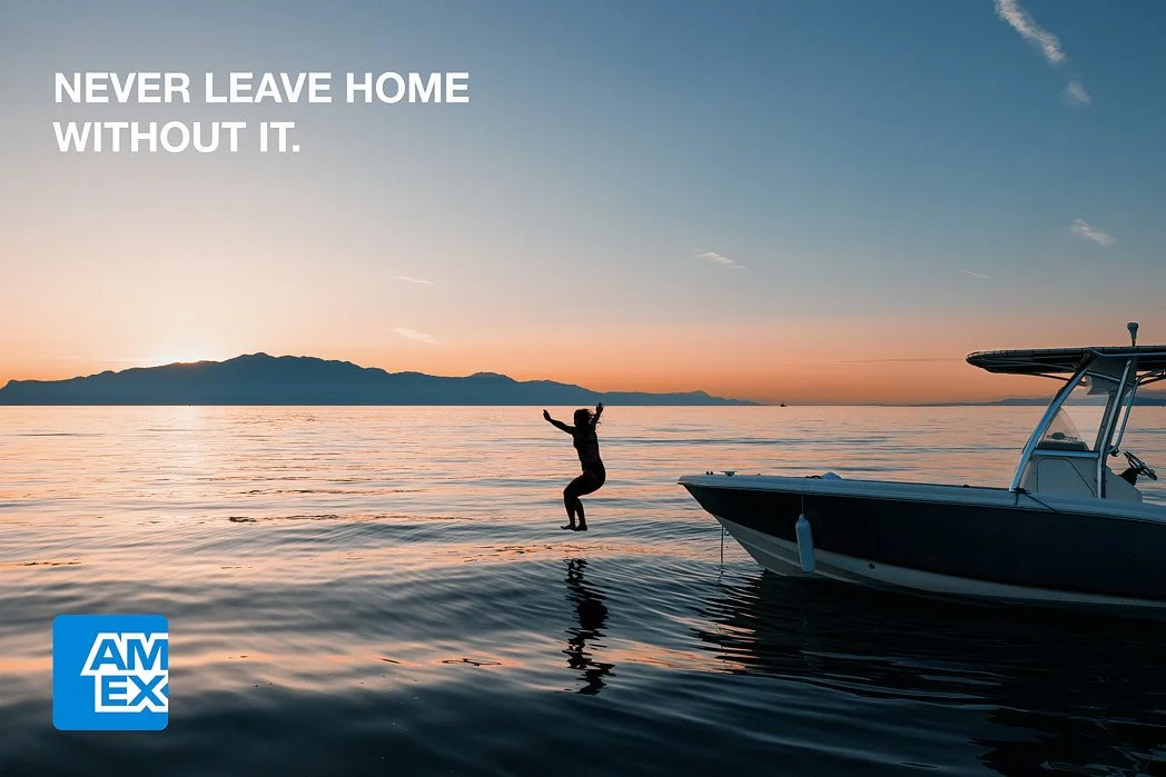 Advertising photographer London campaign image for speculative American Express ad of silhouette actress jumping off boat into ocean at sunset with mountains in background.