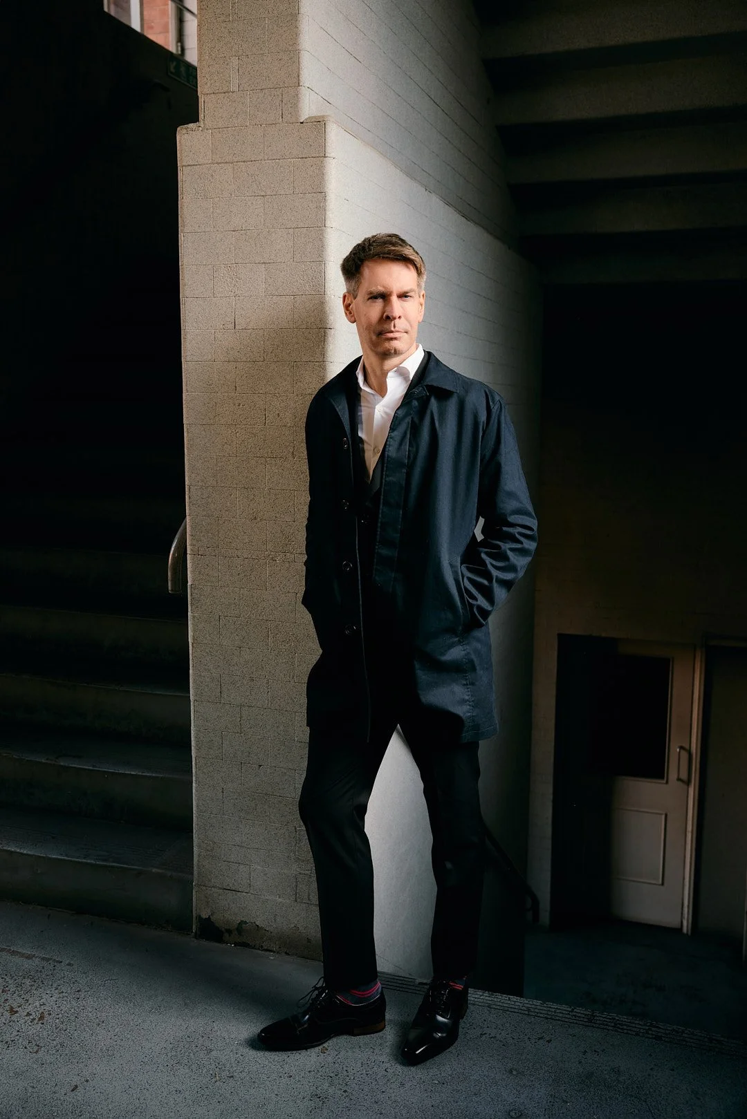 Personal branding photography in dark stairwell with Chris – strong portrait looking off and confident away from camera in London