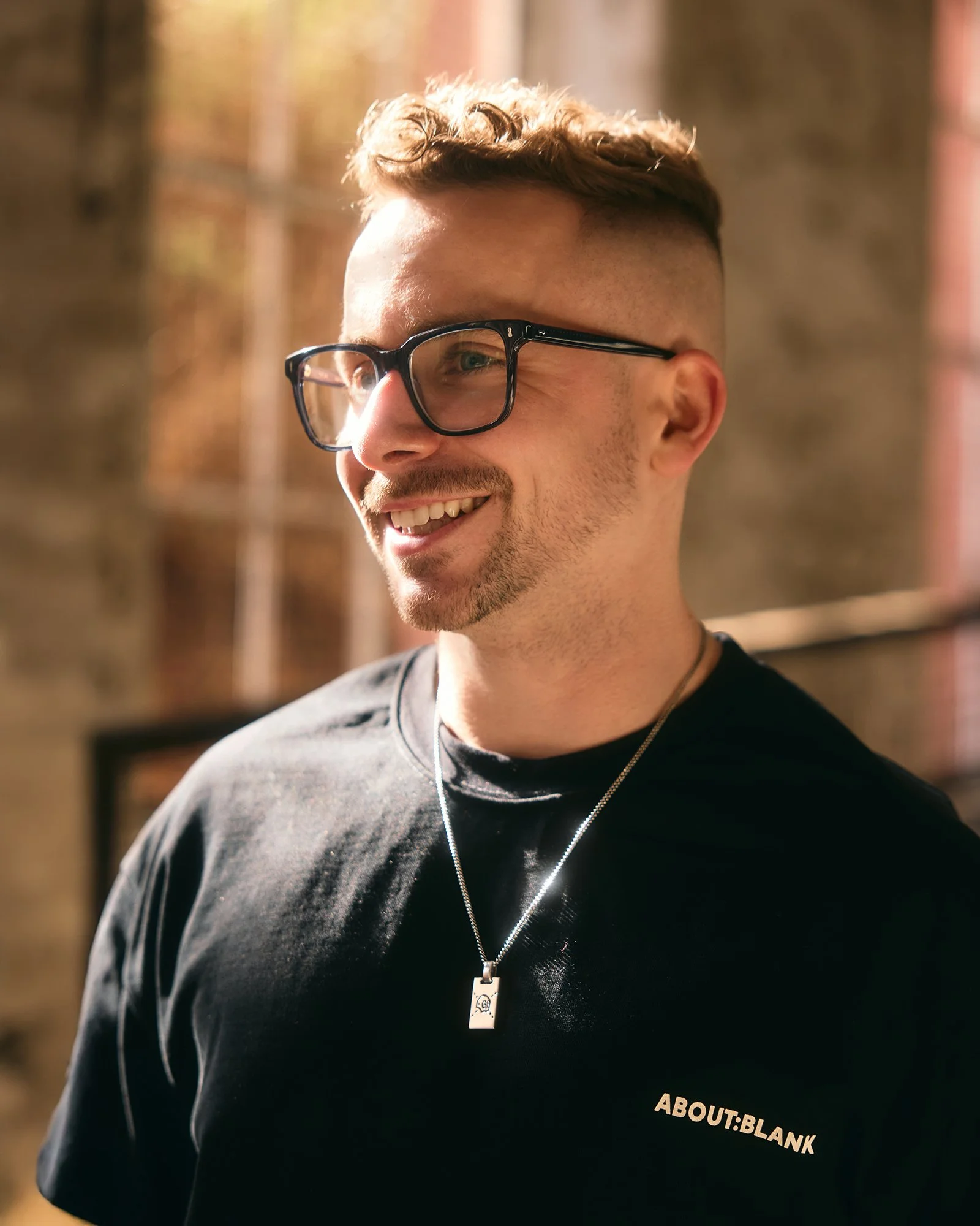 Commercial and advertising photographer in London lifestyle photography portait smiling looking off glasses black shirt and chain