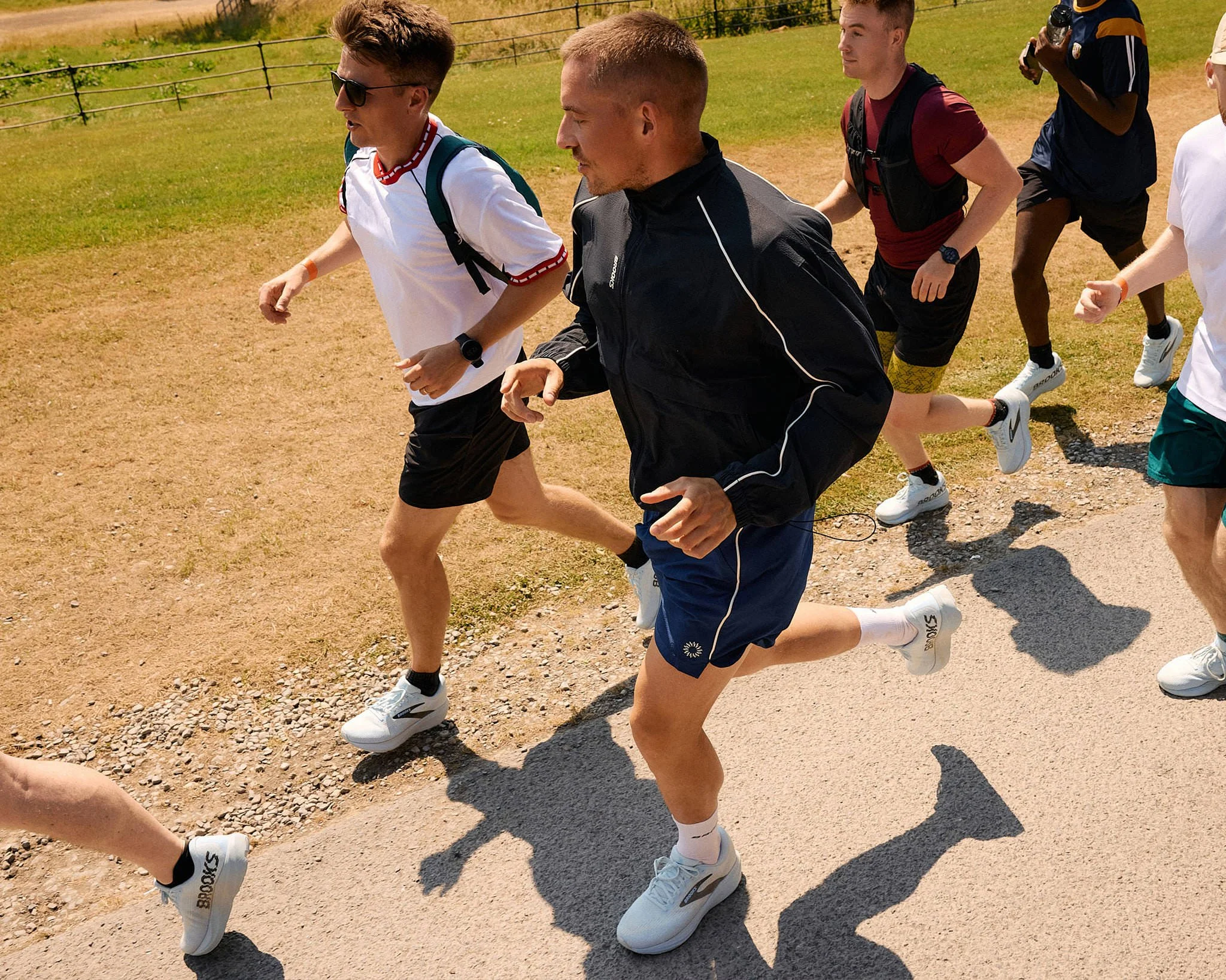 Top-down view of Dermot Kennedy running beside DK5K fans on a sunlit path, shot standing in a moving utility vehicle
