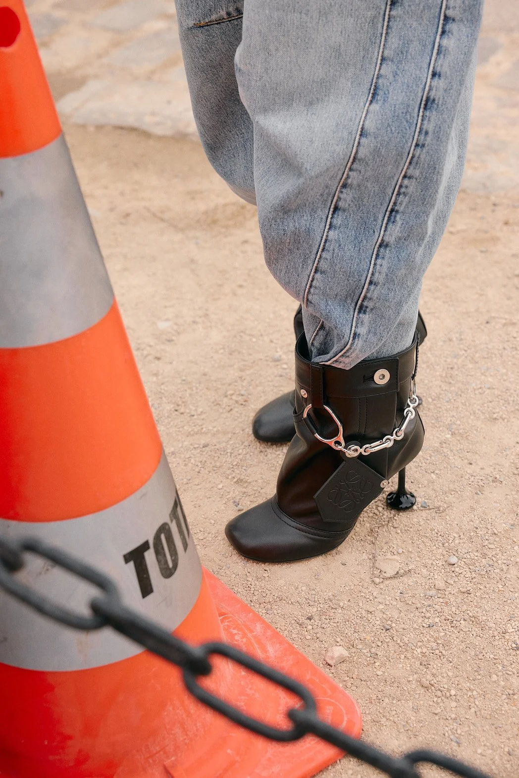 Street style fashion photography at Paris Fashion Week womenswear FW26 by London street photographer of Loewe boot outside Loewe show adjacent to orange cone and chain