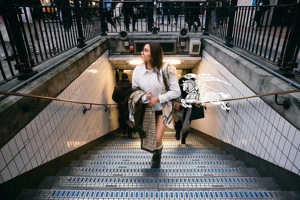 Fashion photographer London street style editorial portrait of Indian influencer Tania Shroff holding Burberry trench coat walking out of Oxford Circus tube station stairs.