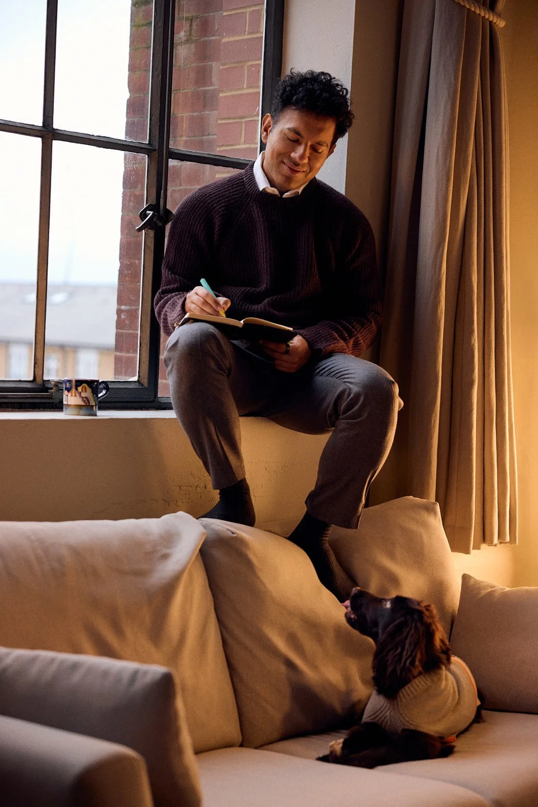 Dating photography portrait of man on windowsill writing on notepad with dog looking up at him