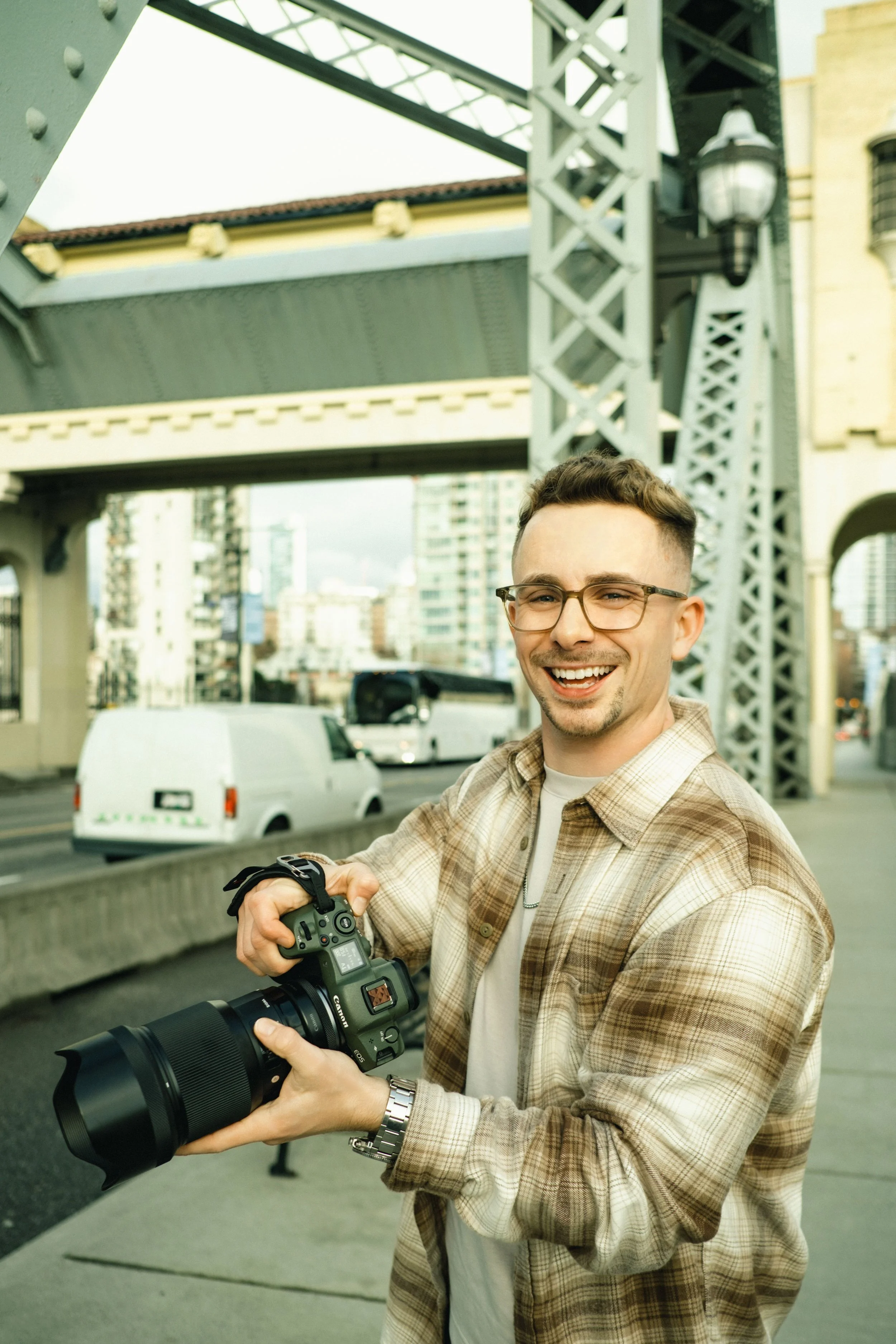 Commercial and advertising photographer in London lifestyle photography portrait smiling holding camera on bridge glasses plaid shirt