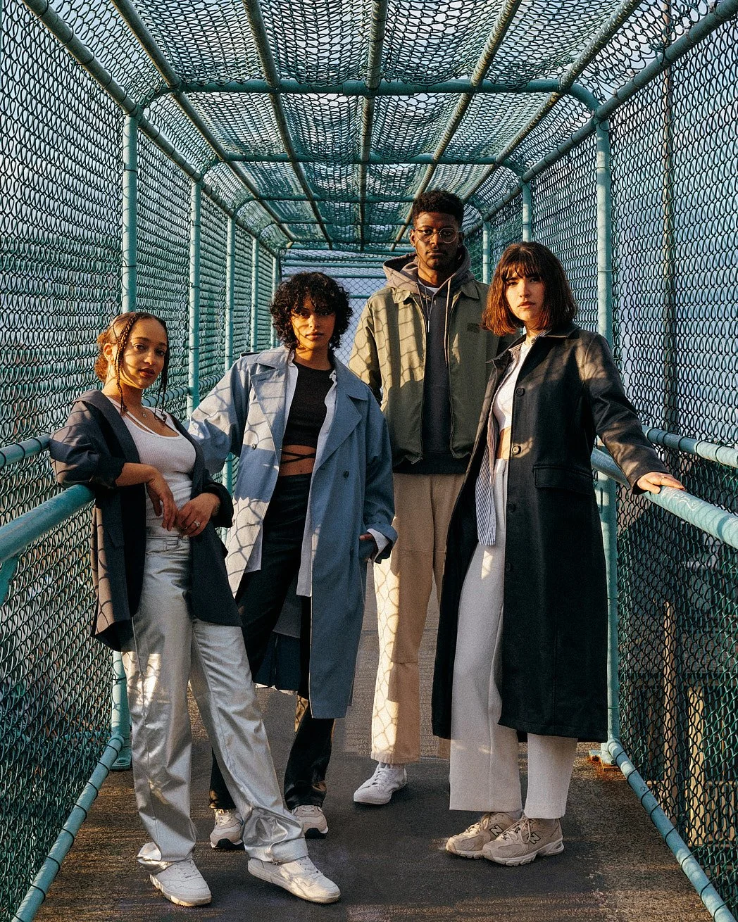 Fashion photographer London editorial image of four models, male and female, on an enclosed green fenced bridge styled for a spring summer editorial campaign at golden hour.