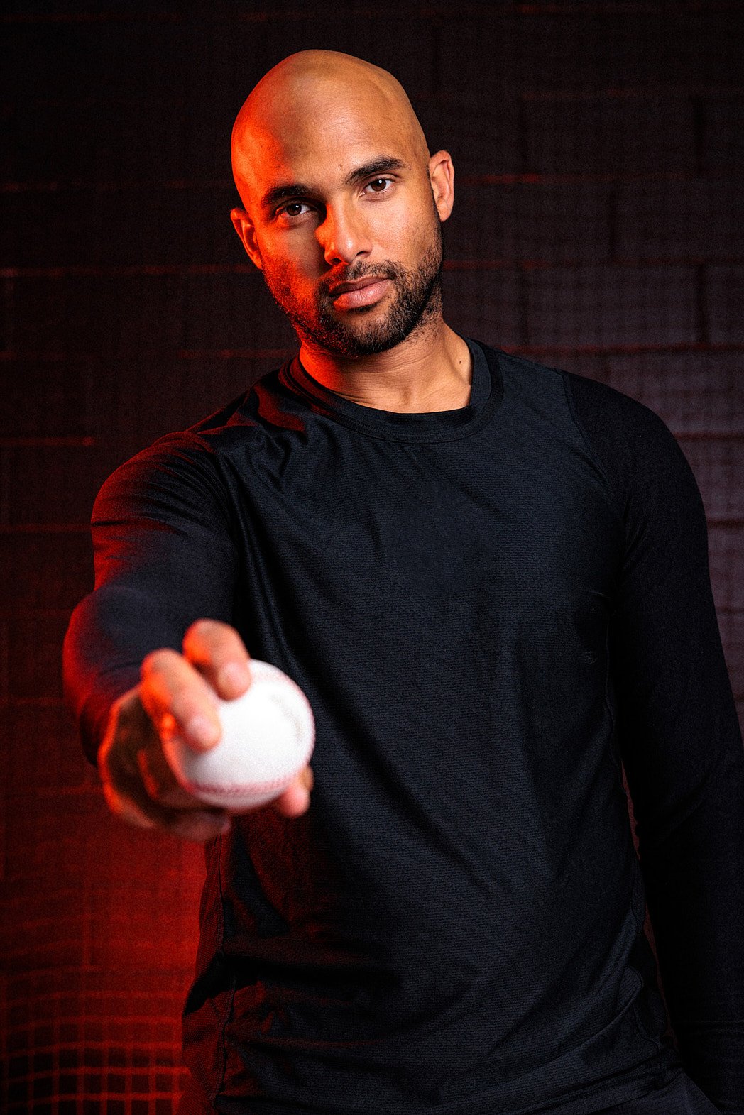 Advertising photographer London commercial lifestyle photography of a baseball coach posing in the studio with a baseball in hand with red light accent and background for a public relations press release campaign for ESPN