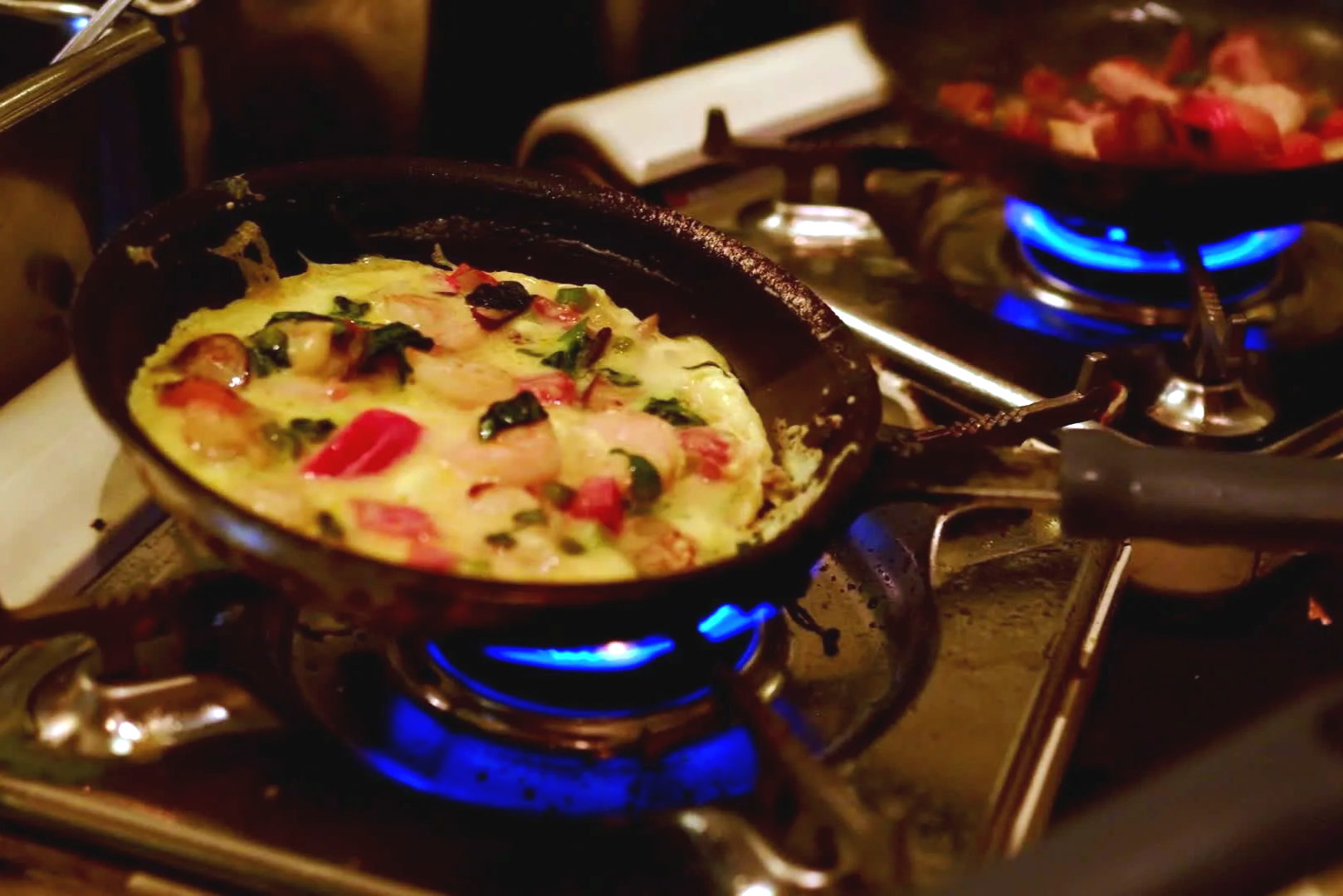 Fried or baked egg dish with peppers and greens cooking on a stove in a cast-iron skillet.