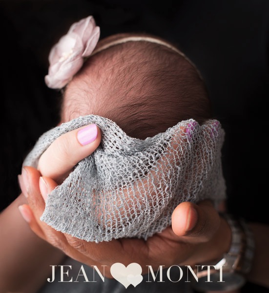Detail of a newborn’s head being held by the hands of her father and mother.