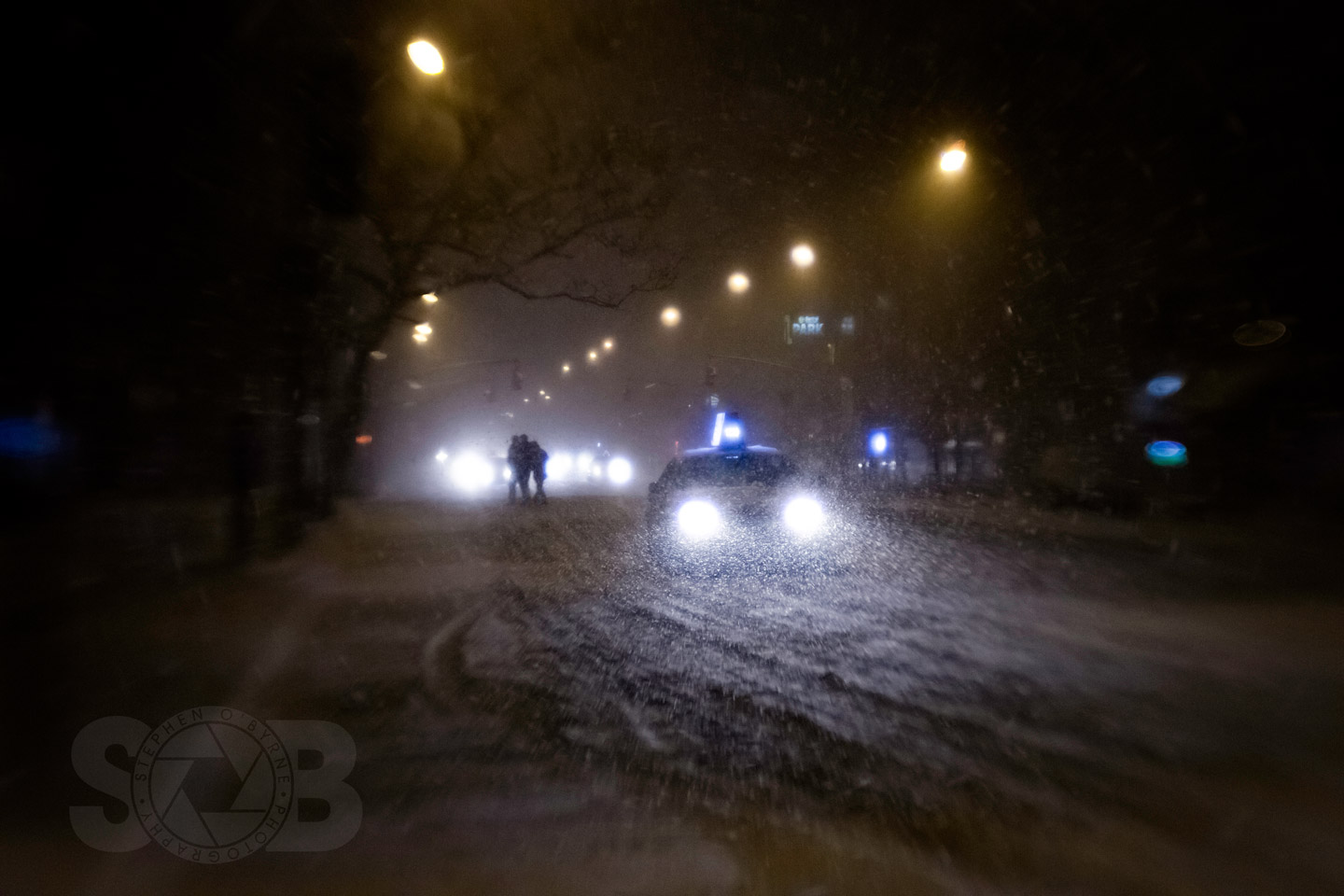 Taxi passes stranded pedestrians during an NYC blizzard.