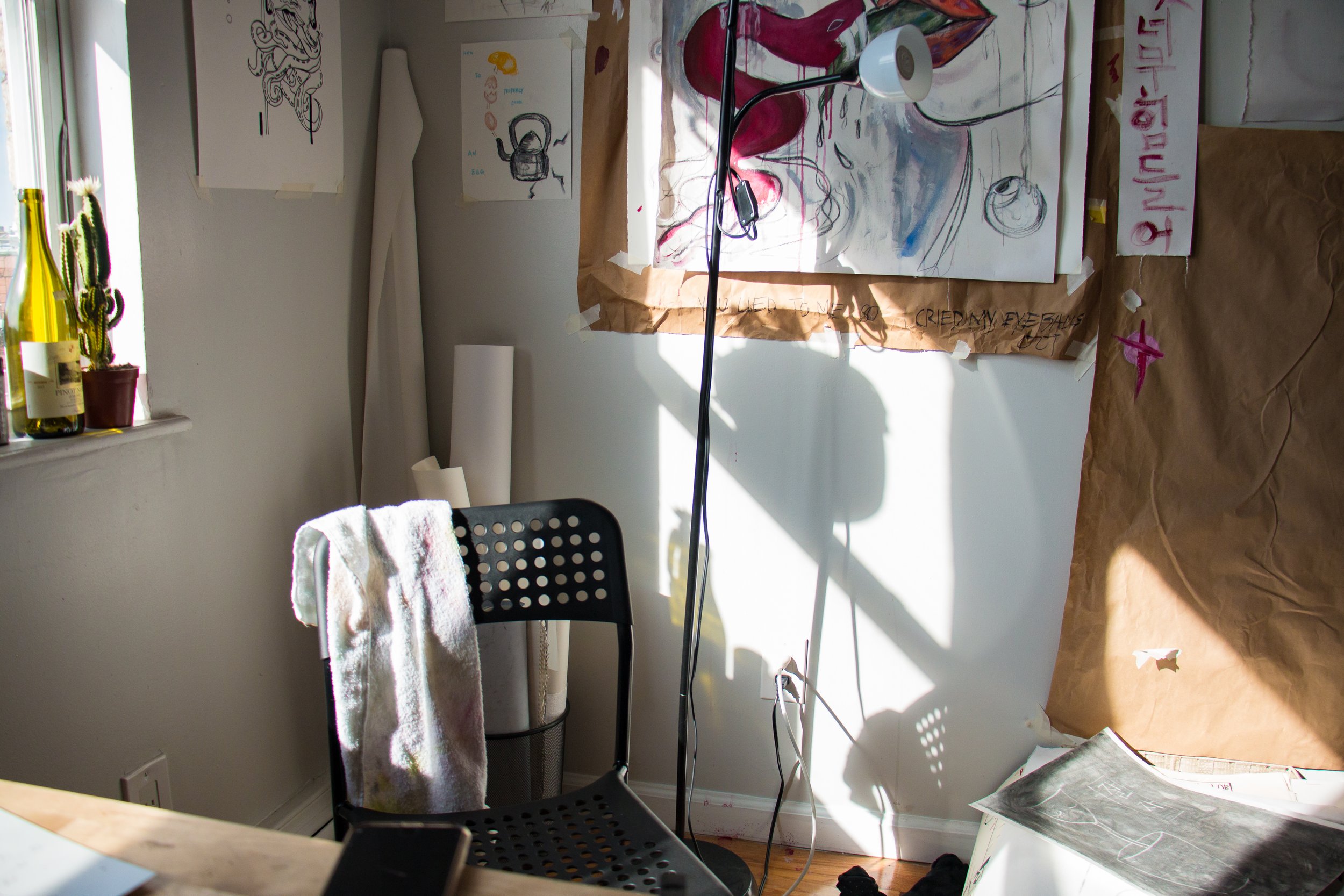 Photo of a chair with a paint-covered towel over it. Behind the chair can be seen a wall covered in artwork and a lamp