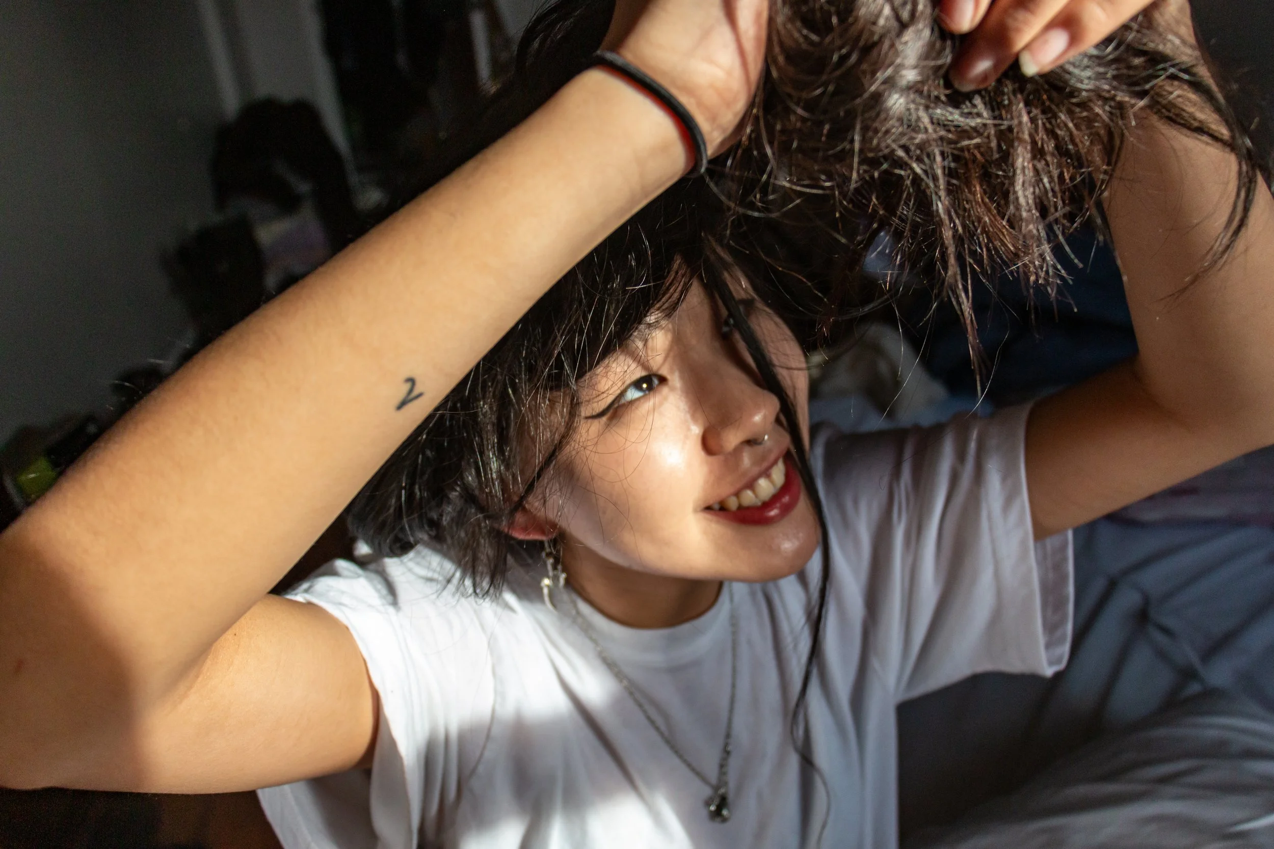 Young korean woman smiling as she untangles her hair. Bushick, NYC. Natural Lighting