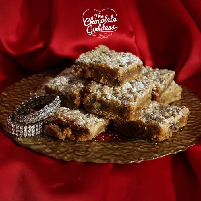 Blonde Bombshells
Those glamorous blonde temptations, I am sure you can all think of one. The Chocolate Goddess introduces you to the latest blonde bombshell - the one with a chocolate walnut and caramel filling. She will be an icon once you taste her. Ladies and gentlemen will prefer this Blondie to all the rest! Ingredients ¾ cup Melted Unsalted Butter (1 ½ sticks) 2 cups packed Brown Sugar 3 large Eggs (lightly whisked) 2 teaspoons Pure Vanilla Extract 3 cups of All Purpose Flour 1 teaspoon Baking Soda 1 teaspoon Salt 1 – 1lb. 1 oz. ounce jar of Butterscotch Caramel sauce (I used Mrs. Richardson’s©) 1 cup Semisweet Chocolate Chips ½ cup roughly chopped Walnuts Confectioner’s Sugar for dusting Baking Instructions - Preheat oven to 350 degrees. Spray a 9 x 13 pan with Butter flavored nonstick cooking spray. - Combine dry ingredients and set aside. - Melt butter and combine using mixer with brown sugar, eggs and vanilla. - Add dry ingredients and combine thoroughly. Mixture will be crumbly. - Press half the mixture into pan. Bake 6 minutes. - Remove from oven and pour on caramel sauce. Sprinkle with chocolate chips and walnuts. - Top with remaining mixture. It will resemble crumbs on a cupcake. - Bake another 20 – 22 minutes until edges are just golden brown. - Cool and then refrigerate 3 hours until set. Let stand at room temperature before cutting. - Makes 20 Blonde Bombshells. Store in airtight plastic container for up to 5 days.