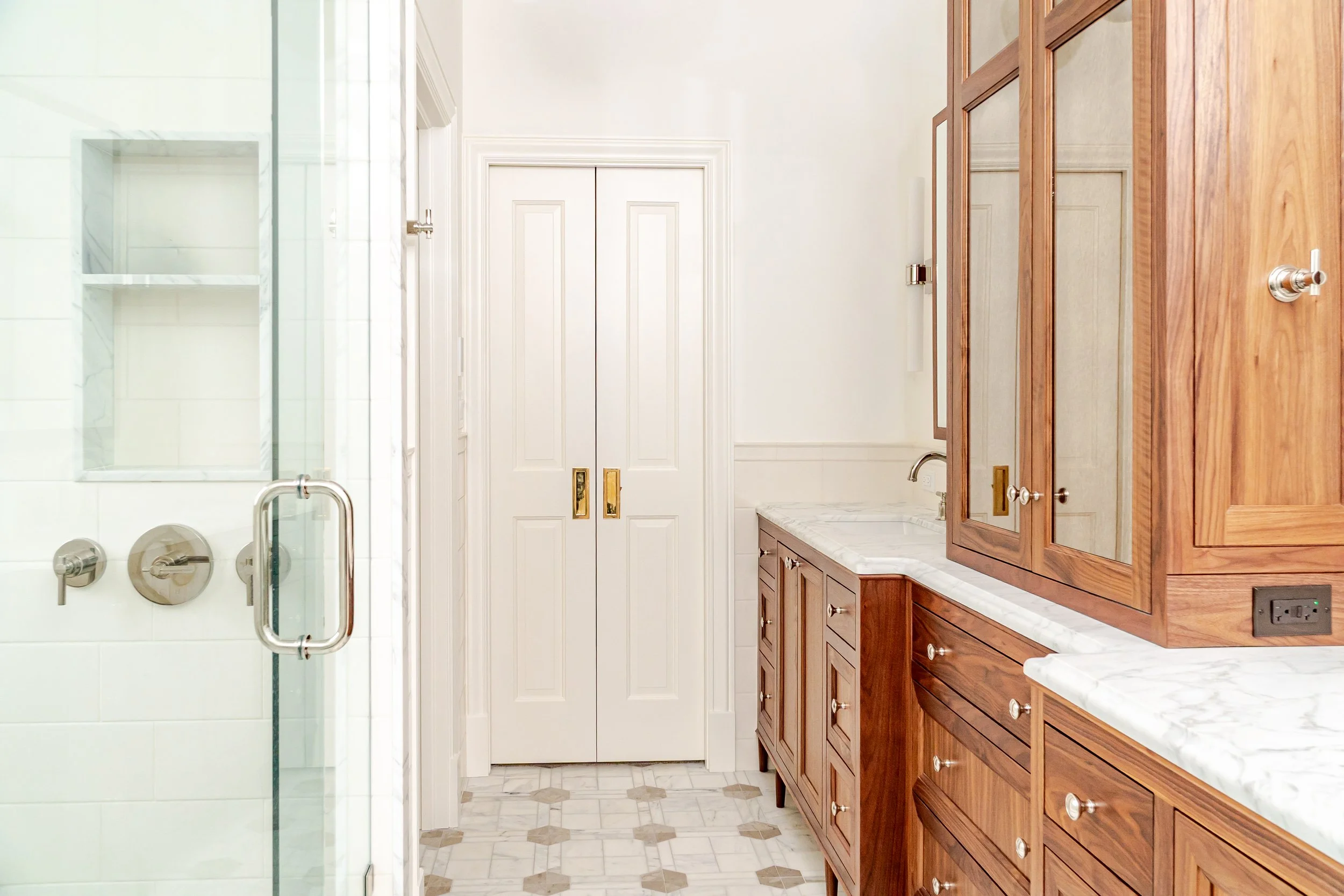 Bathroom with wooden cabinets, marble countertop, and a glass shower door.