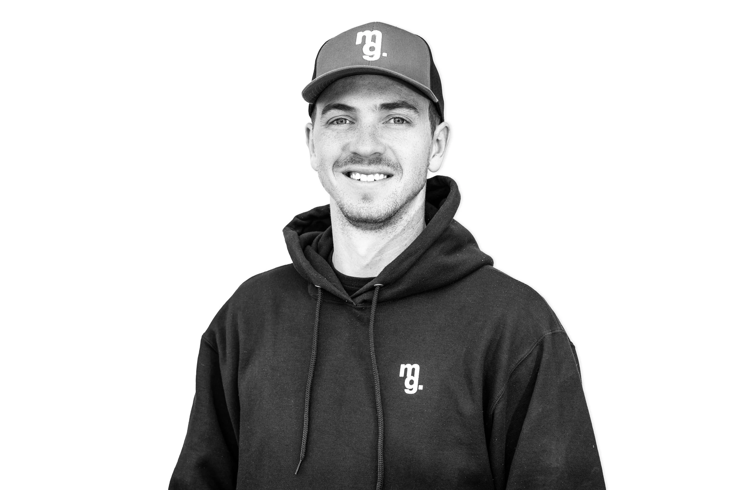 Black and white photo of a young man wearing a baseball cap and hoodie, smiling at the camera.