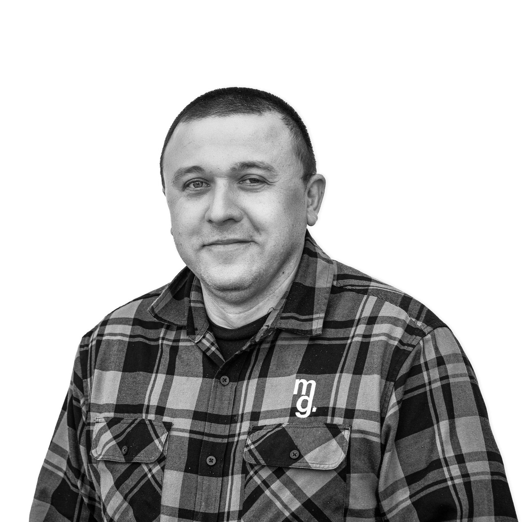 Black and white photo of a man with short hair, wearing a plaid shirt with a logo on the chest, smiling subtly, against a plain white background.