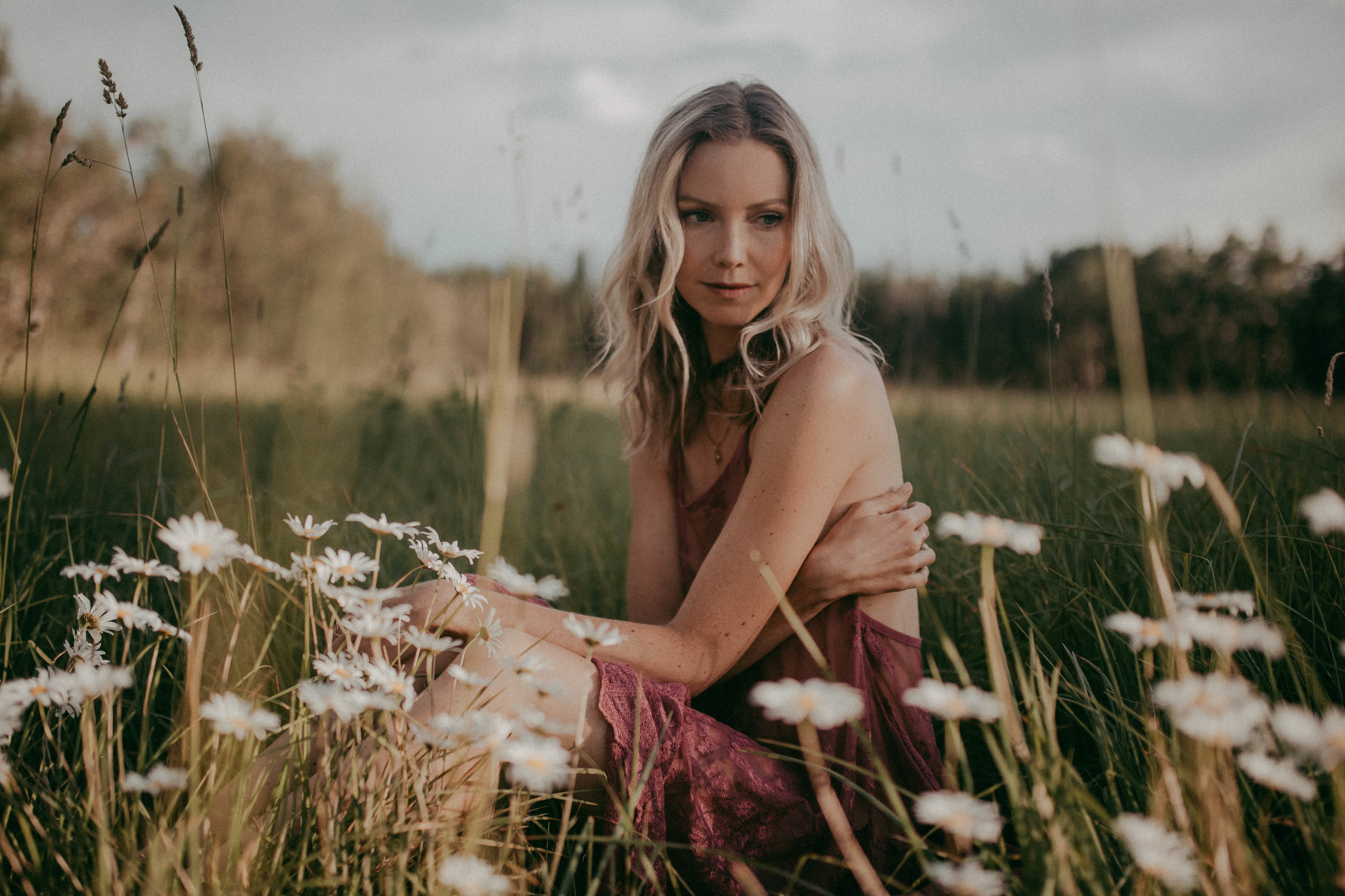Woman sitting in a field with white daisies, wearing a purple dress